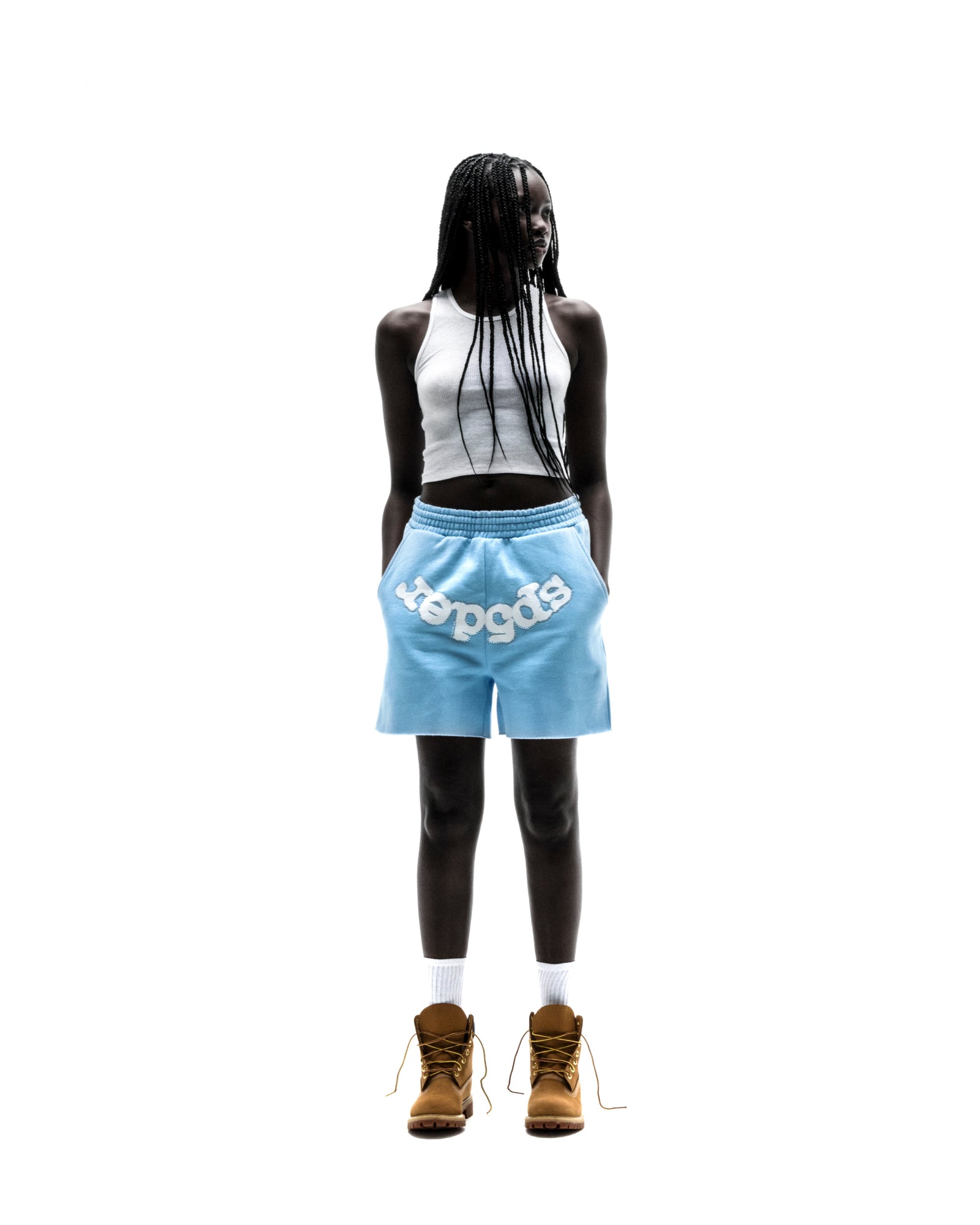 Model in light blue OG WEB SWEATSHORTS with "SP5DER" text, white crop top, and brown boots.