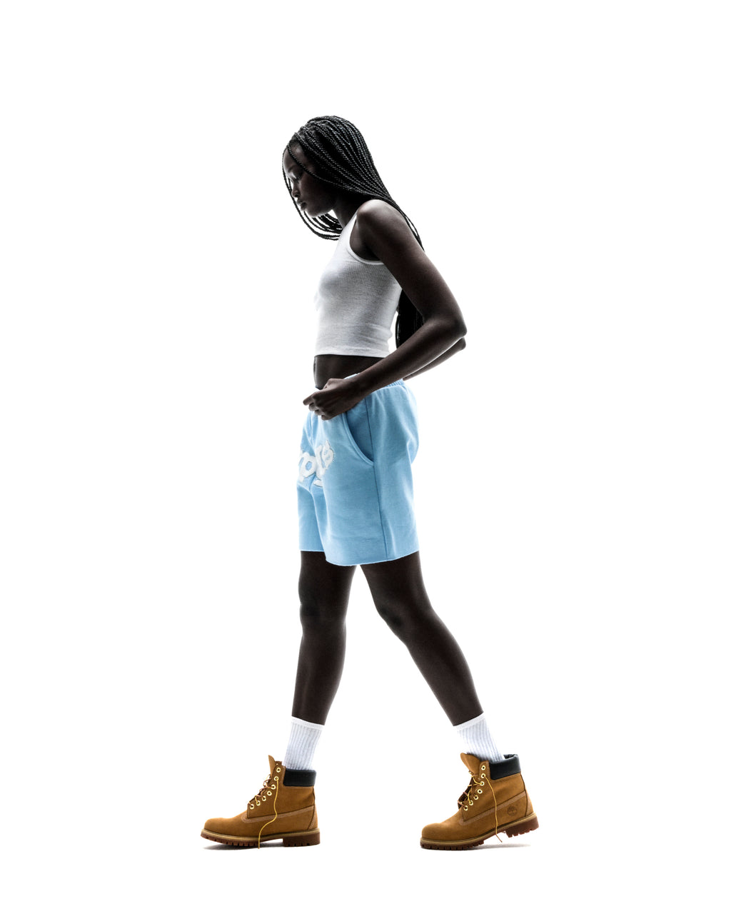Model in light blue OG WEB SWEATSHORT with "SP5DER" print, white tank top, and tan boots.