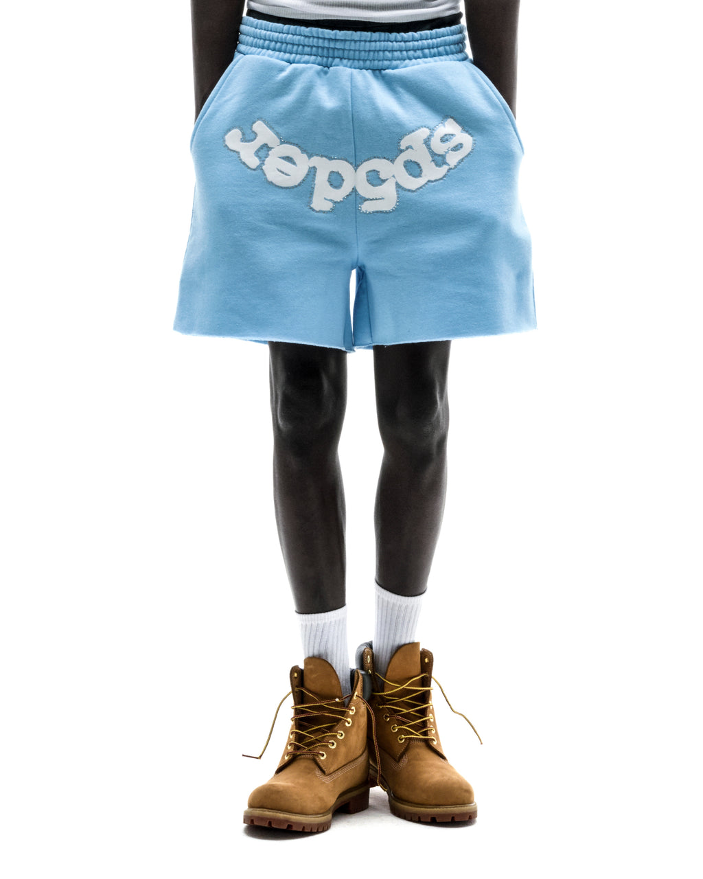 Model wearing light blue OG WEB SWEATSHORT with "SP5DER" text, raw hem, and drawcord waistband.