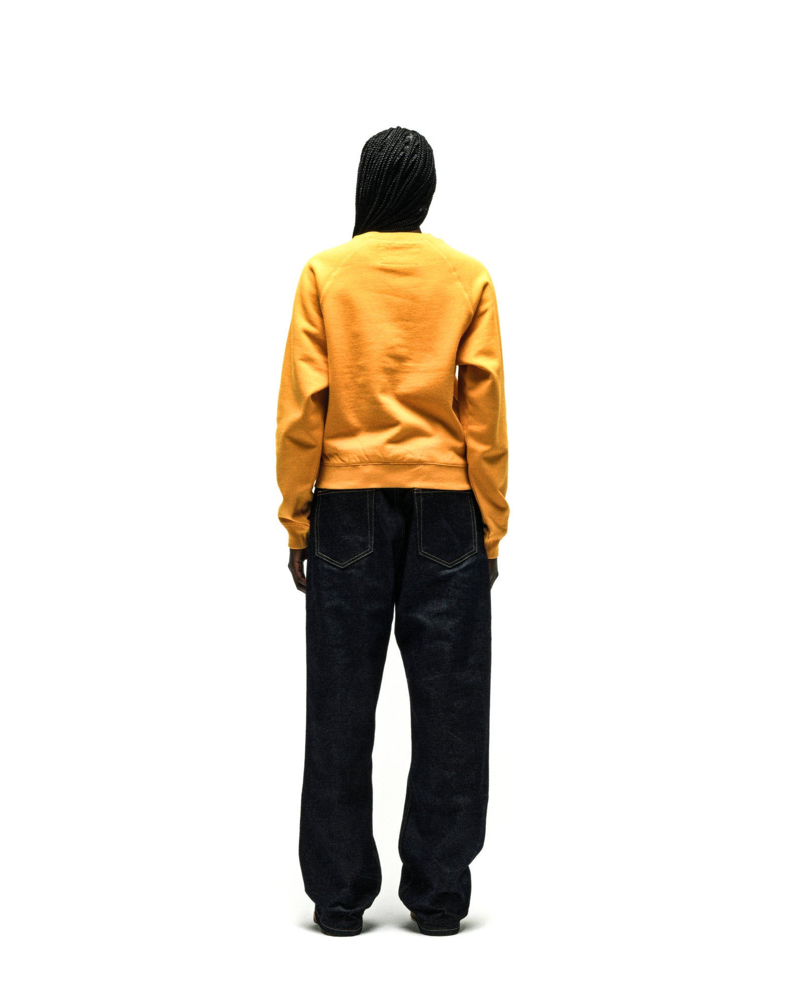 Back view of a yellow 100% cotton brushed fleece raglan crewneck with ribbed cuffs and hem, worn with dark denim jeans.