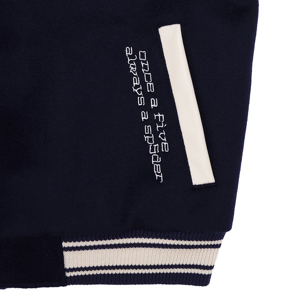 Navy wool varsity jacket sleeve with white cowhide trim, "once a five always a spider" embroidery, and striped knit cuff.