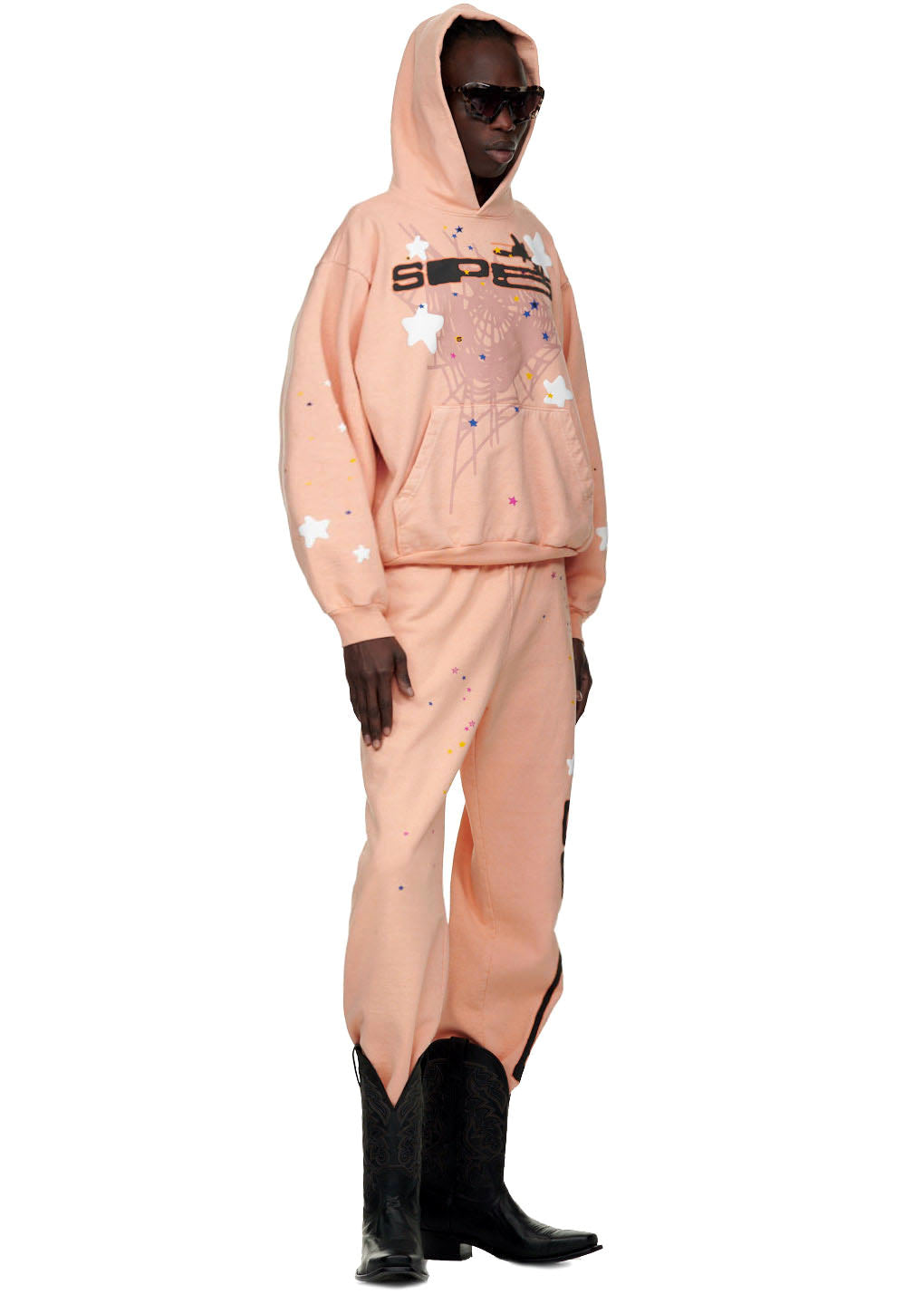 Male model in a peach SP5 Bellini hoodie and matching sweatpants with web/star puff prints.