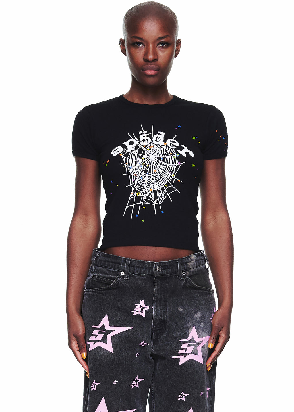 Female model in black OG WEB V2 BABY TEE with white spiderweb graphic and colorful stars, paired with black jeans.