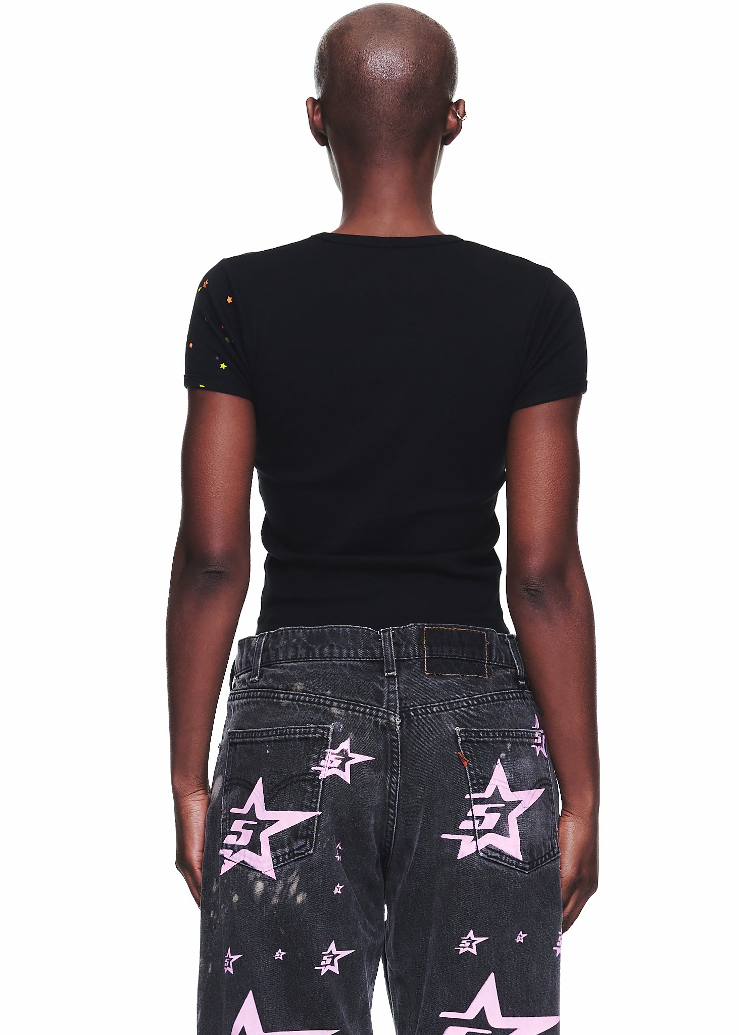 Back view of a female model wearing a black cropped fitted cotton baby tee with colorful star details on the sleeve.