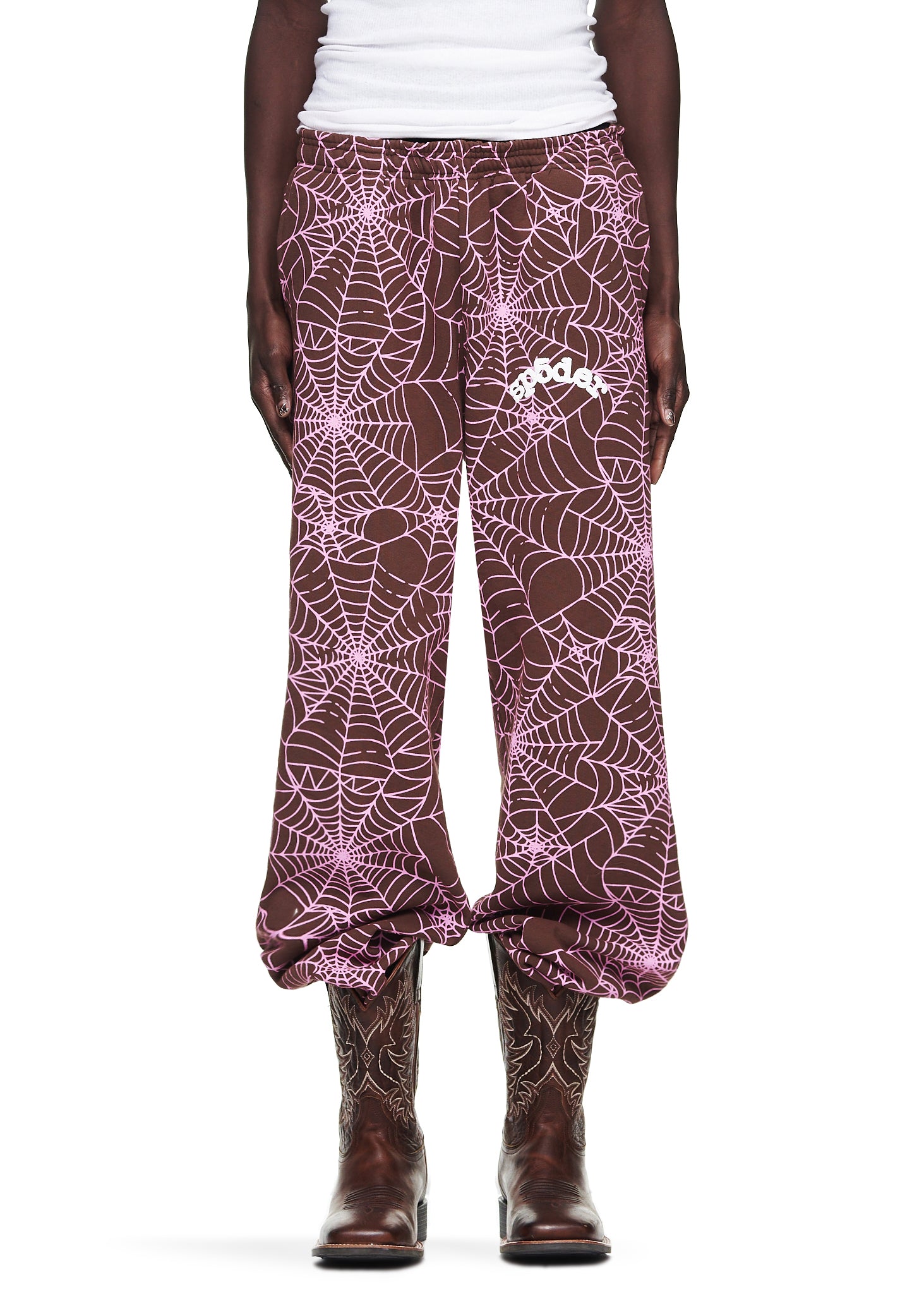 Brown fleece sweatpants with all-over pink cracked web print and "SP5DER" text, worn by a male model.
