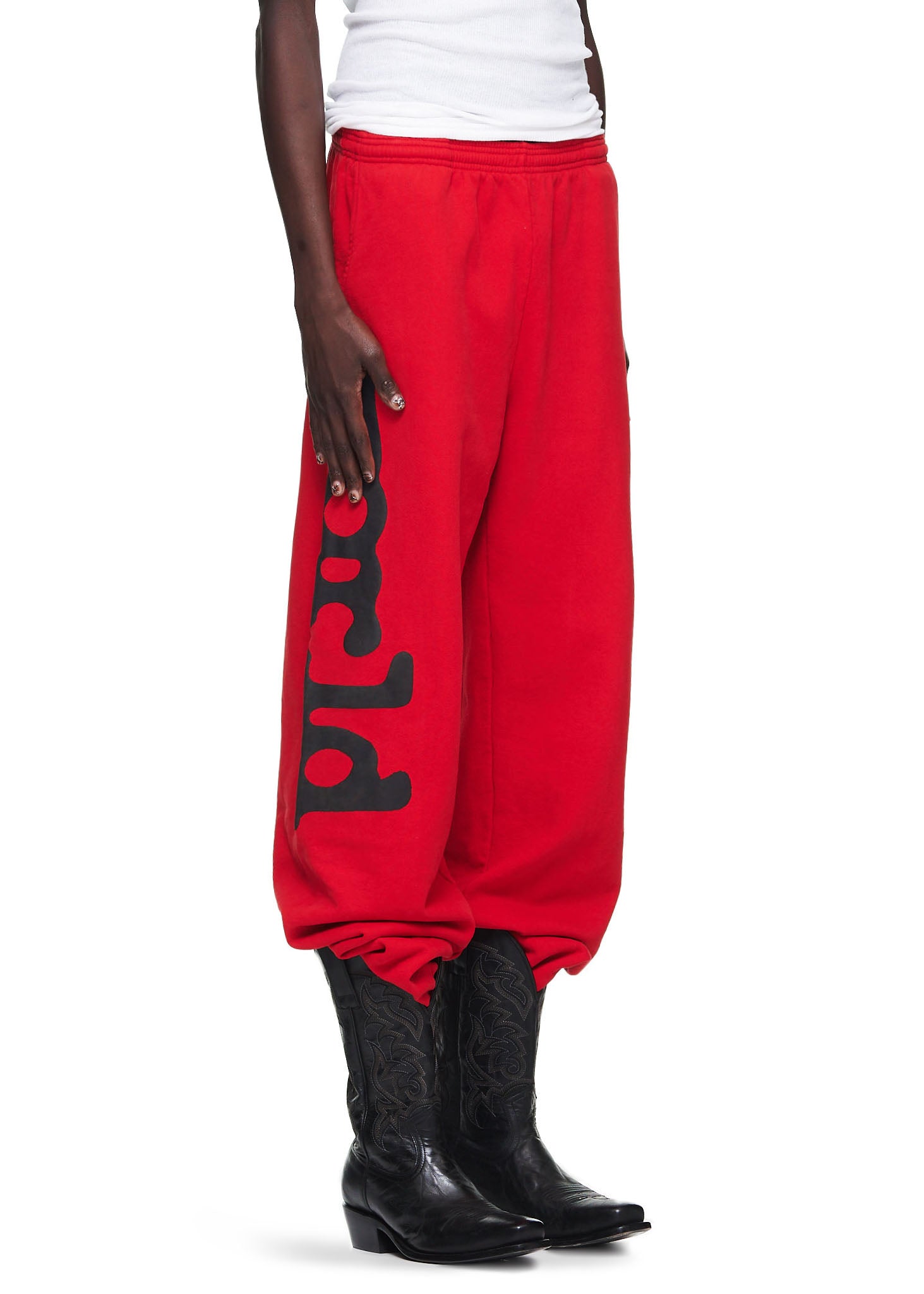 Red Beluga sweatpants with black puff print, worn by a male model with cowboy boots.