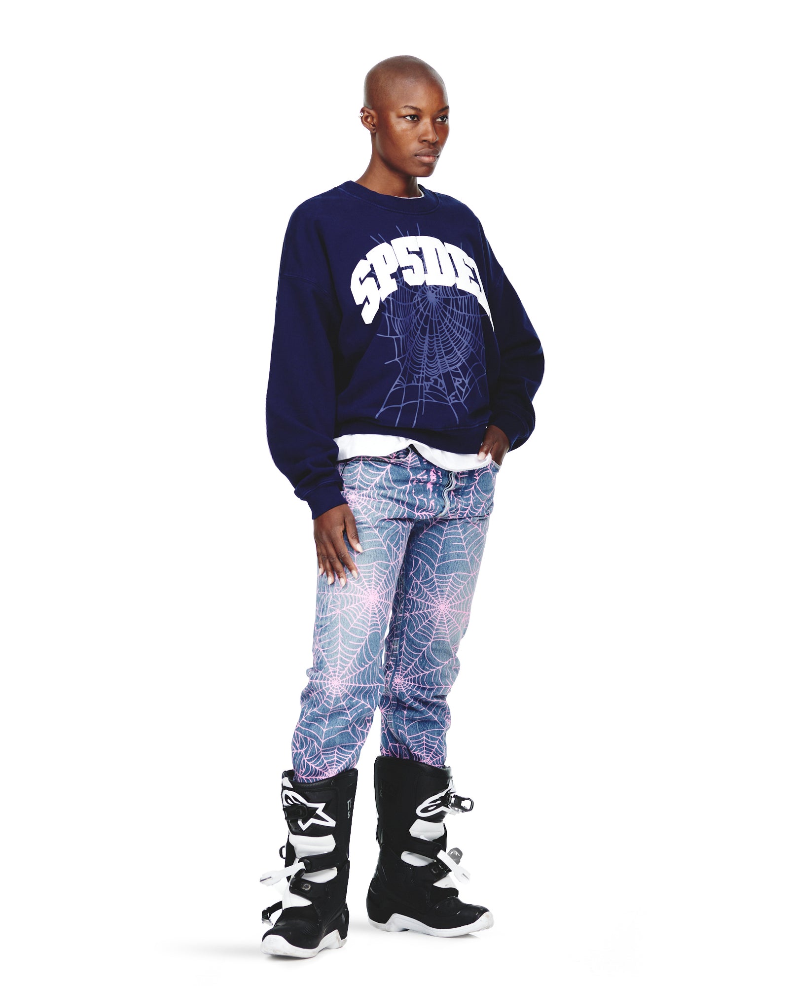 Male model in a navy VARSITY WEB CREWNECK with white spiderweb graphic, light blue web-print jeans, and black boots.
