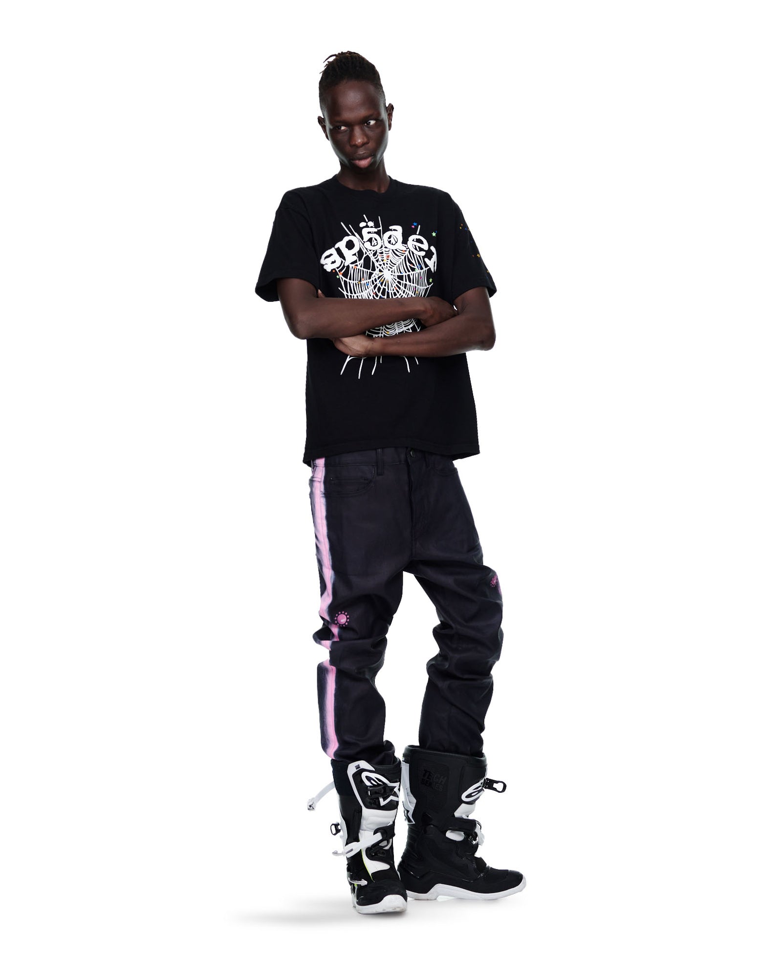 Male model in black cotton OG web print tee, dark jeans with pink stripes, and black/white boots.