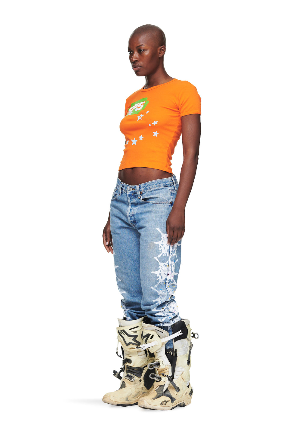 Female model in orange cropped cotton baby tee with green SP5 graphic and white stars.