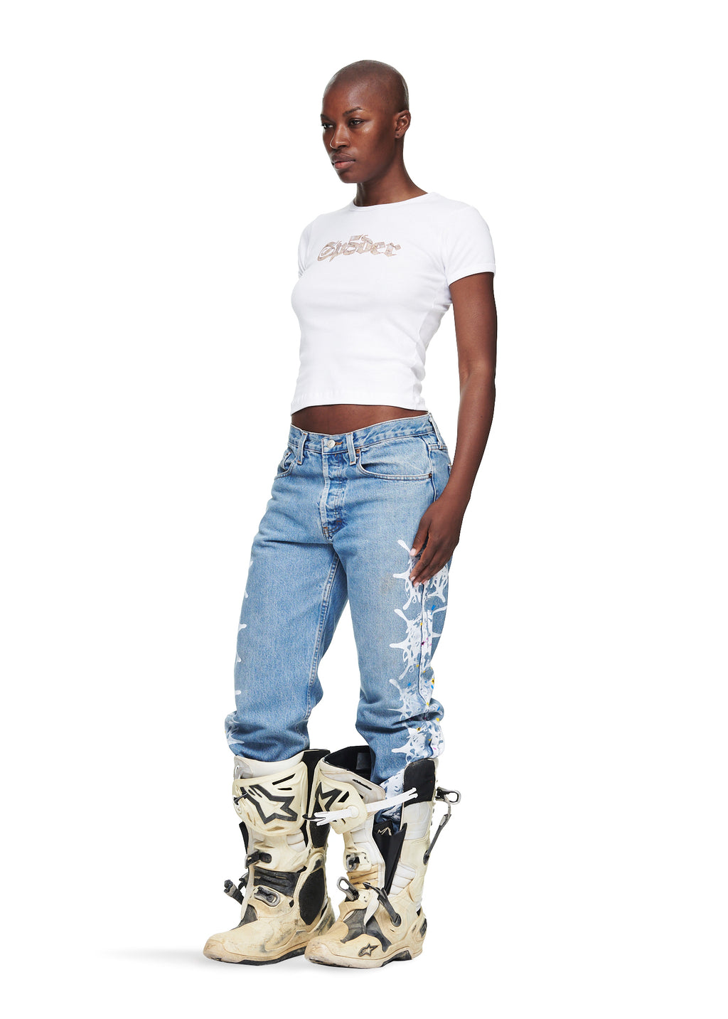 Female model in white cropped cotton tee with graphic print, blue jeans, and motocross boots.