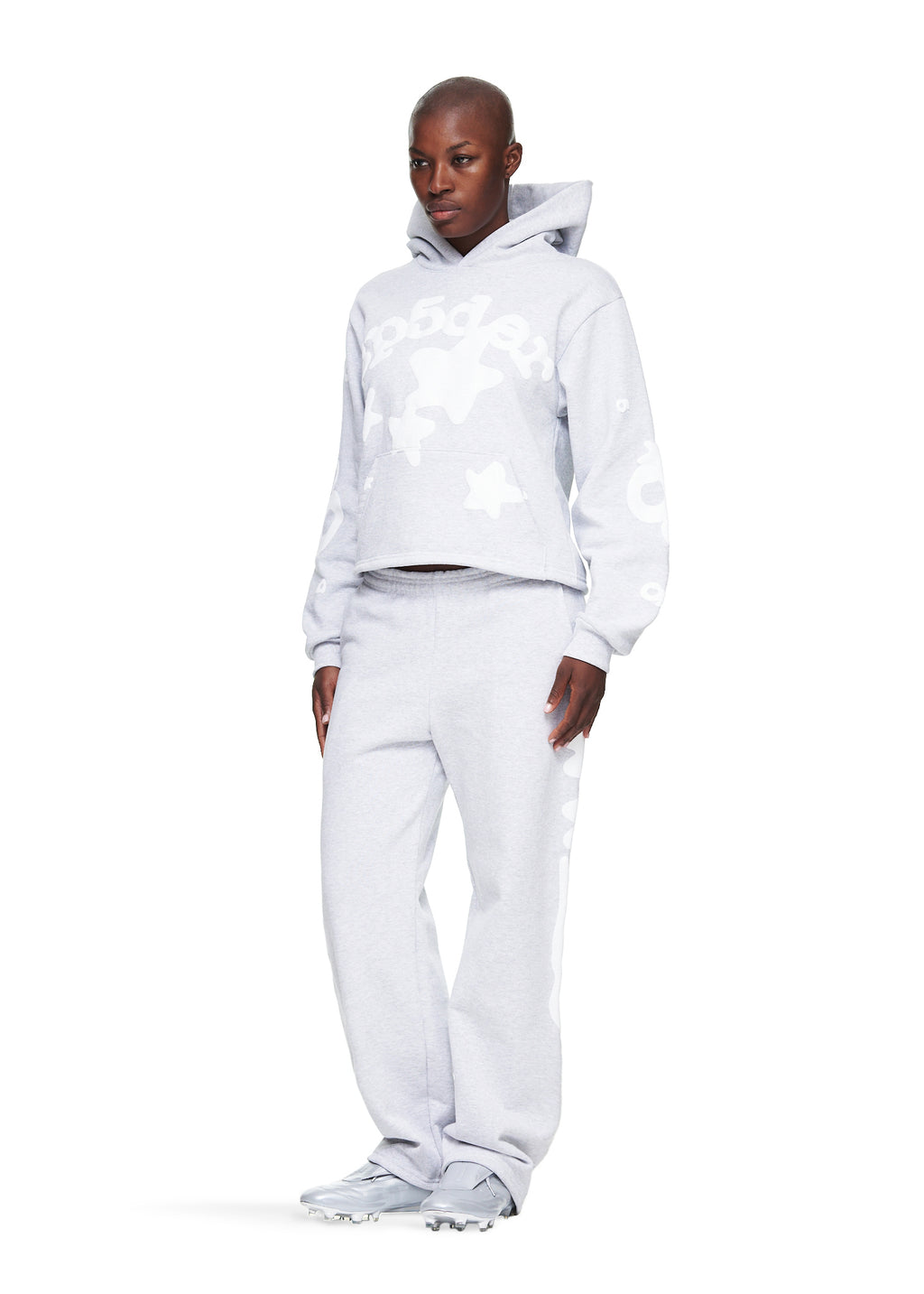 Woman in a cropped grey fleece hoodie and matching sweatpants with 'SP5DER' and star prints.