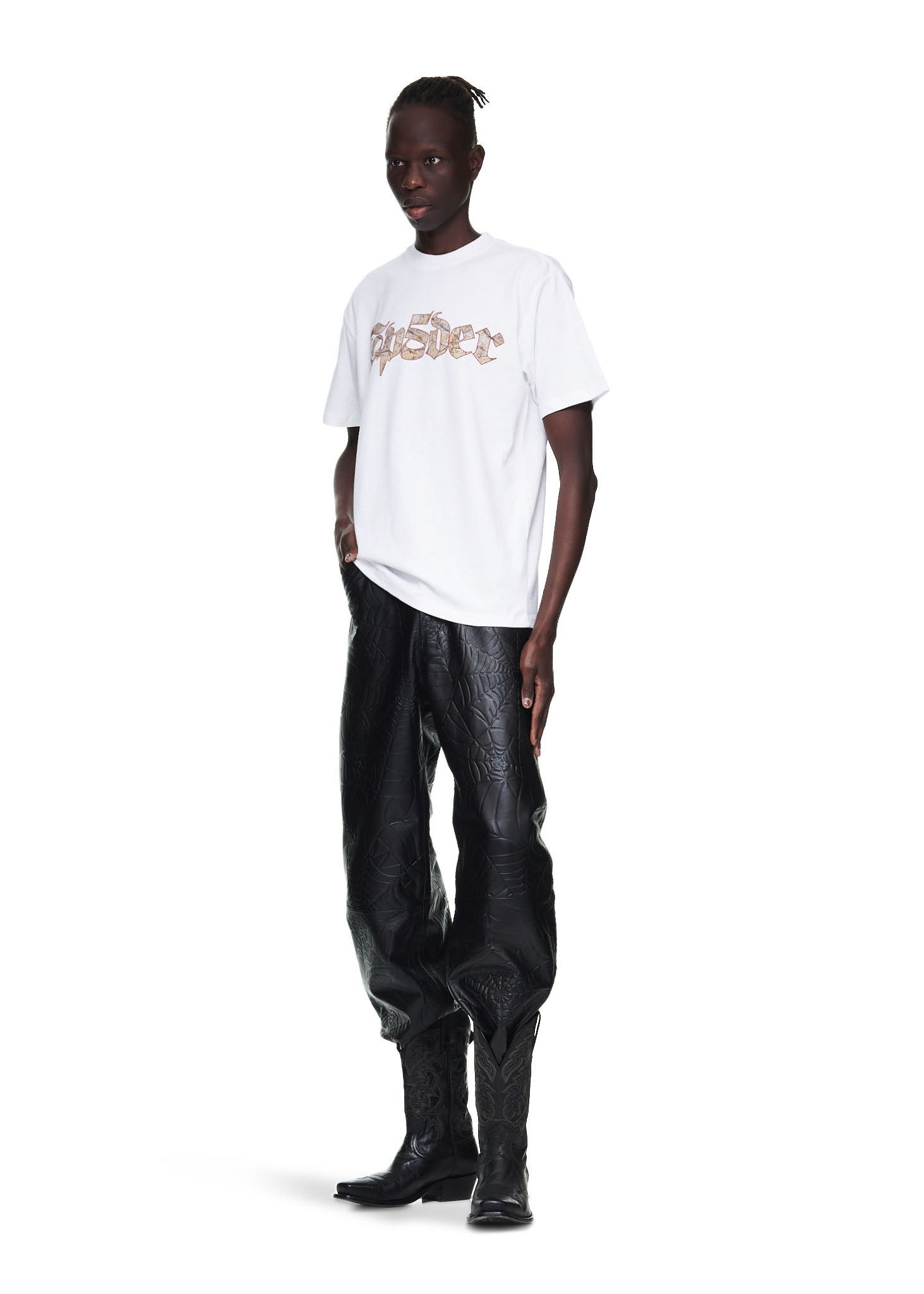 Male model in white 100% cotton WHITE JUAN V2 TEE with graphic print, black pants, and cowboy boots.