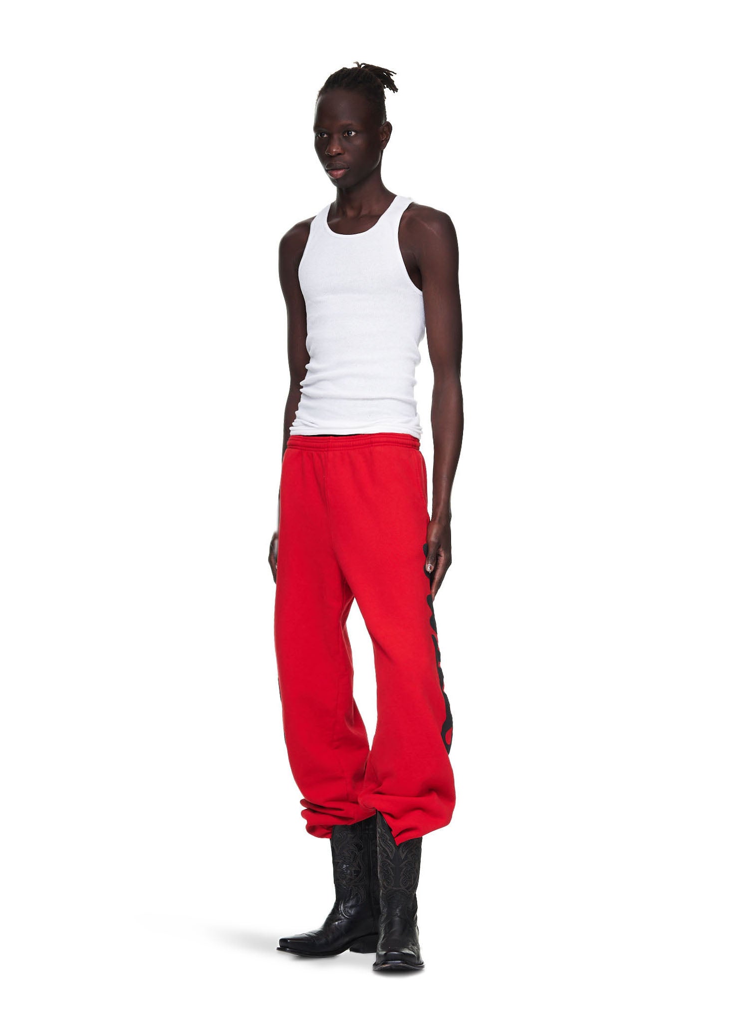 Male model in red fleece sweatpants with "Worldwide" print, paired with a white tank top and black cowboy boots.