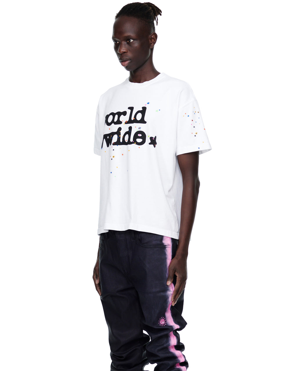 Male model in white 14oz cotton Worldwide tee with colorful stars, wearing dark jeans.