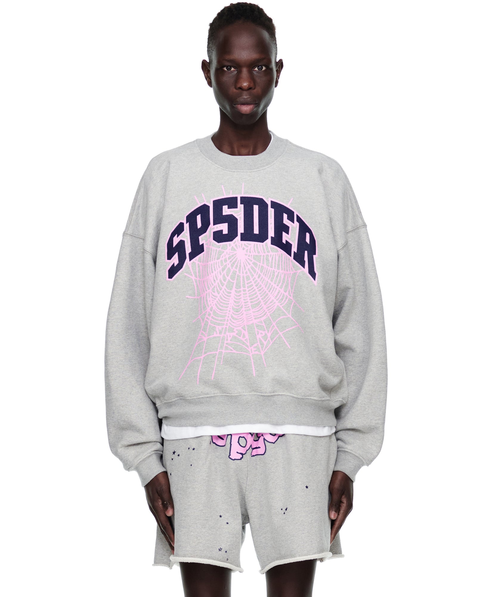 Grey VARSITY WEB CREWNECK with "SP5DER" and pink web print, worn by a model.
