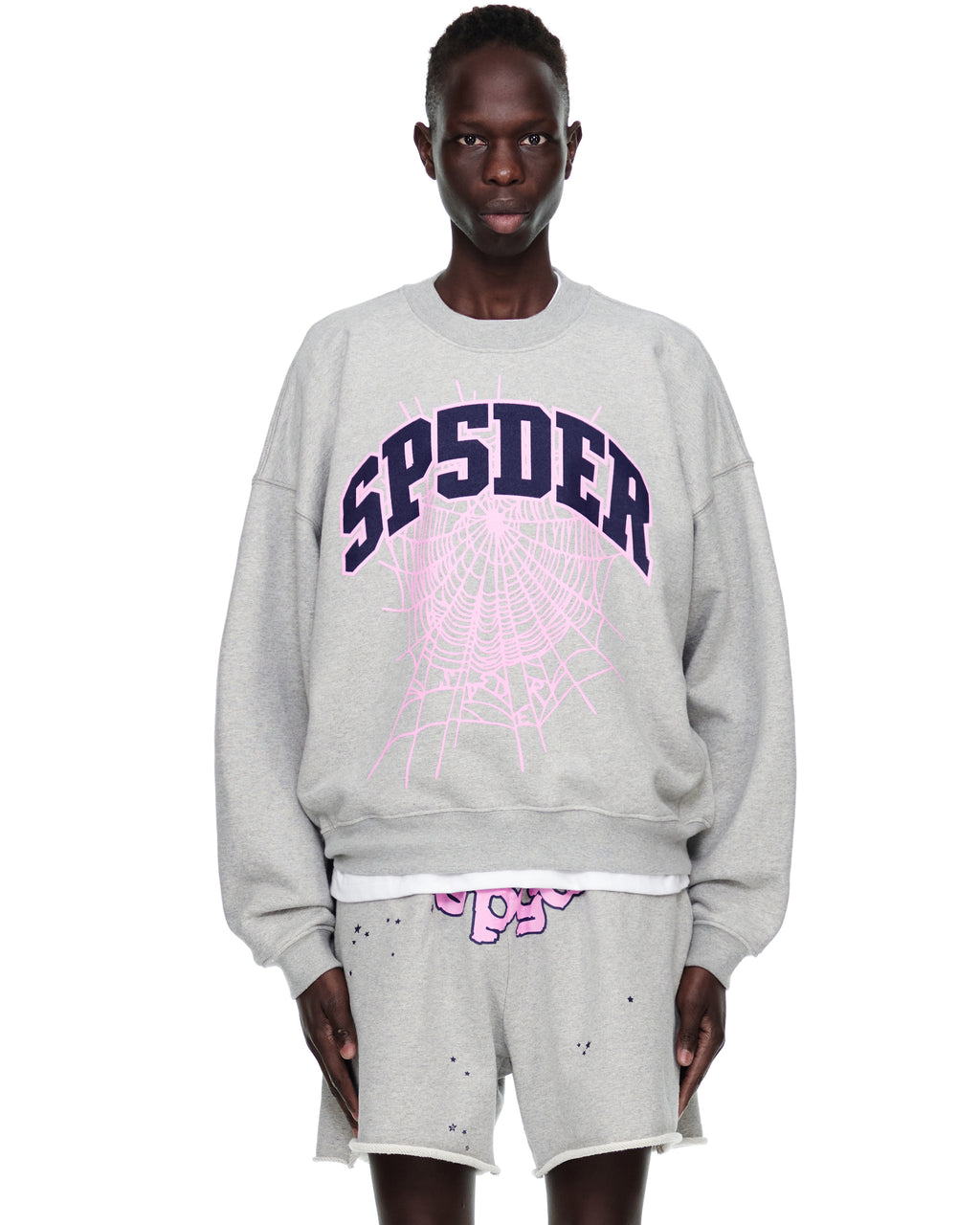 Grey VARSITY WEB CREWNECK with "SP5DER" and pink web print, worn by a model.
