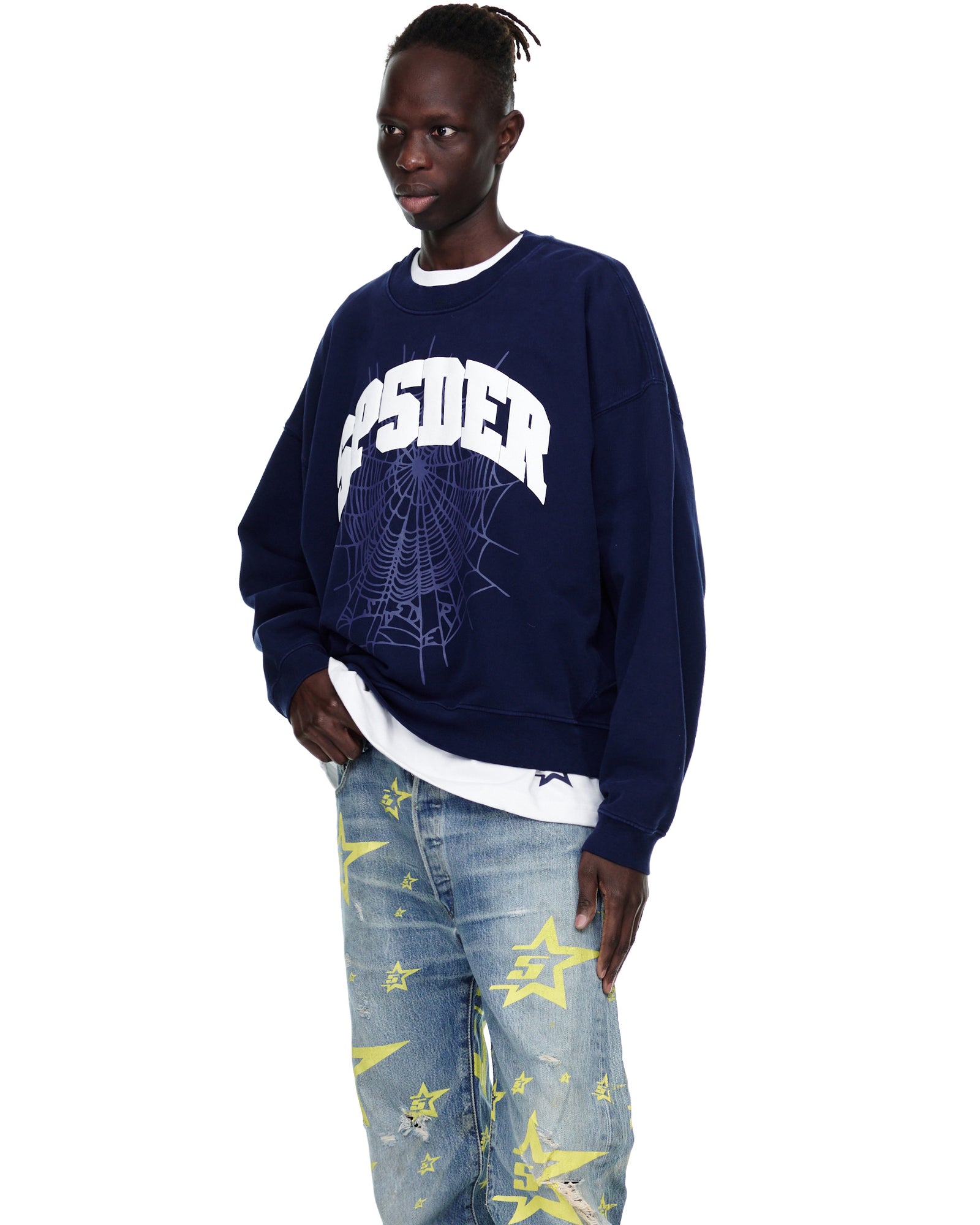 Male model in a navy VARSITY WEB CREWNECK with a white spiderweb graphic, light wash jeans with yellow stars.