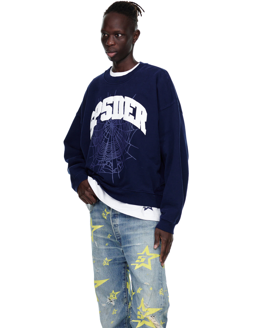 Male model in a navy VARSITY WEB CREWNECK with a white spiderweb graphic, light wash jeans with yellow stars.