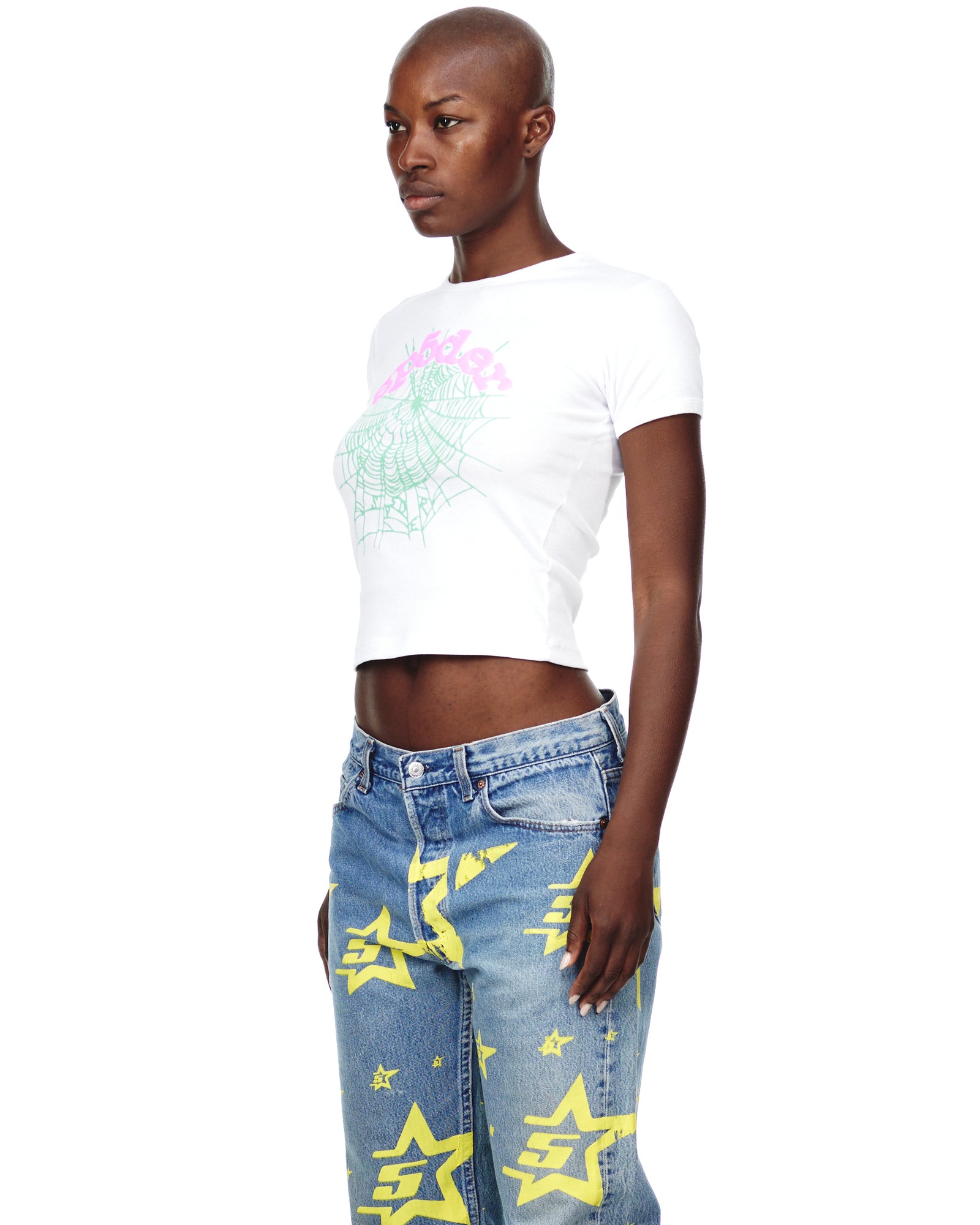 Female model in white cropped OG WEB CANDY BABY TEE with pink and green graphic print, paired with blue jeans.