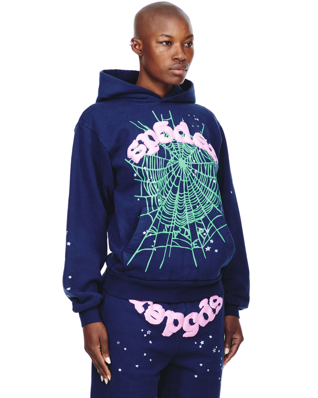 Female model in navy OG WEB HOODIE and matching sweatpants with pink "sp5der" text and green spiderweb print.