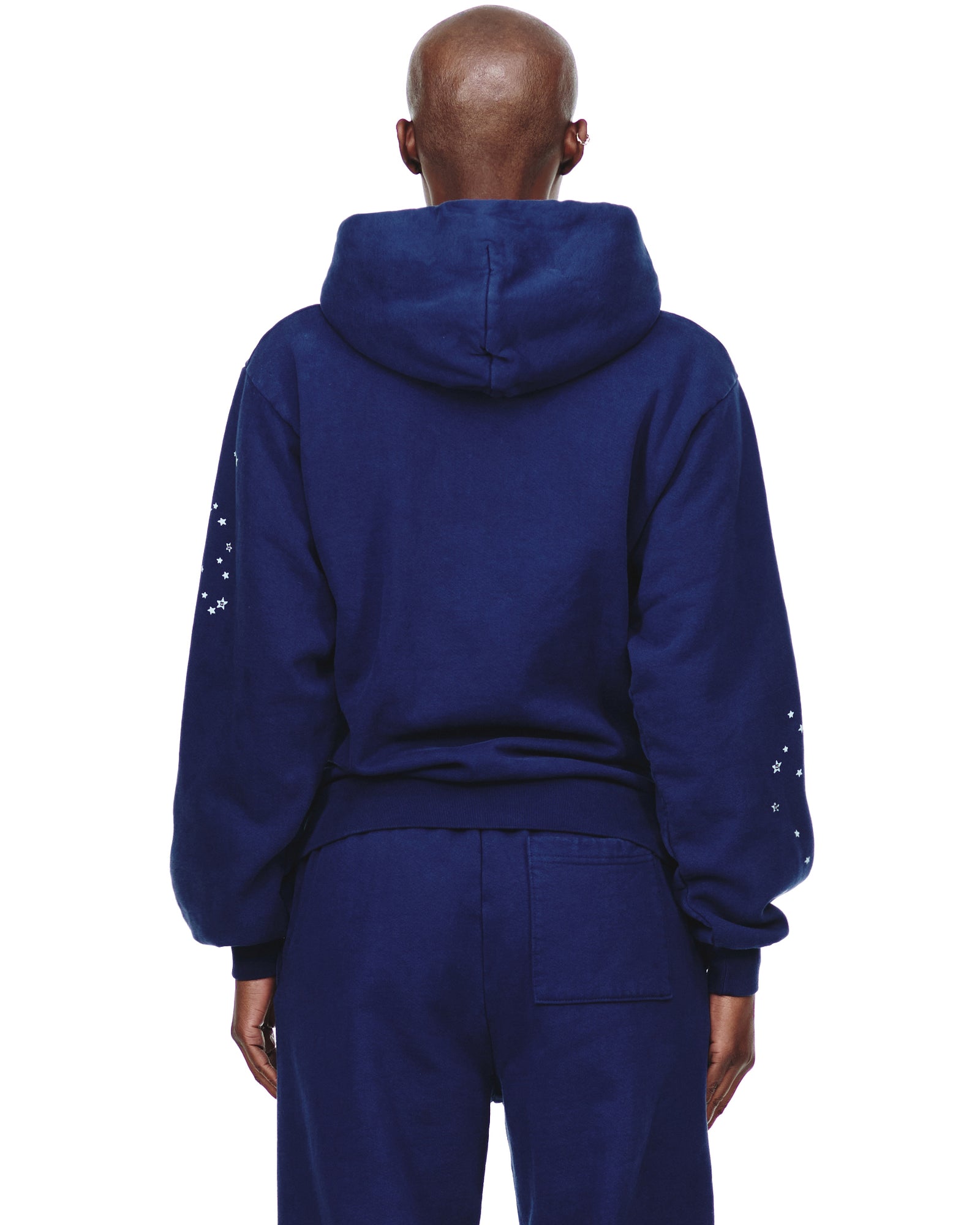 Back of a navy blue 23oz fleece hoodie with white star prints on the sleeves, paired with matching sweatpants.