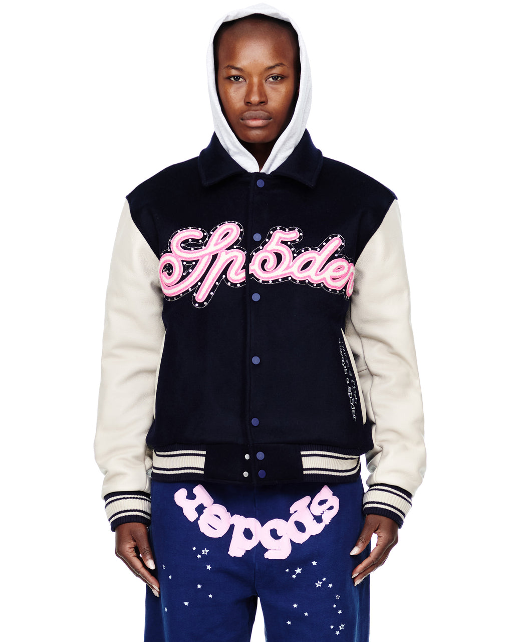 Female model in a navy wool varsity jacket with cream leather sleeves, pink chenille patches, and a white hoodie.