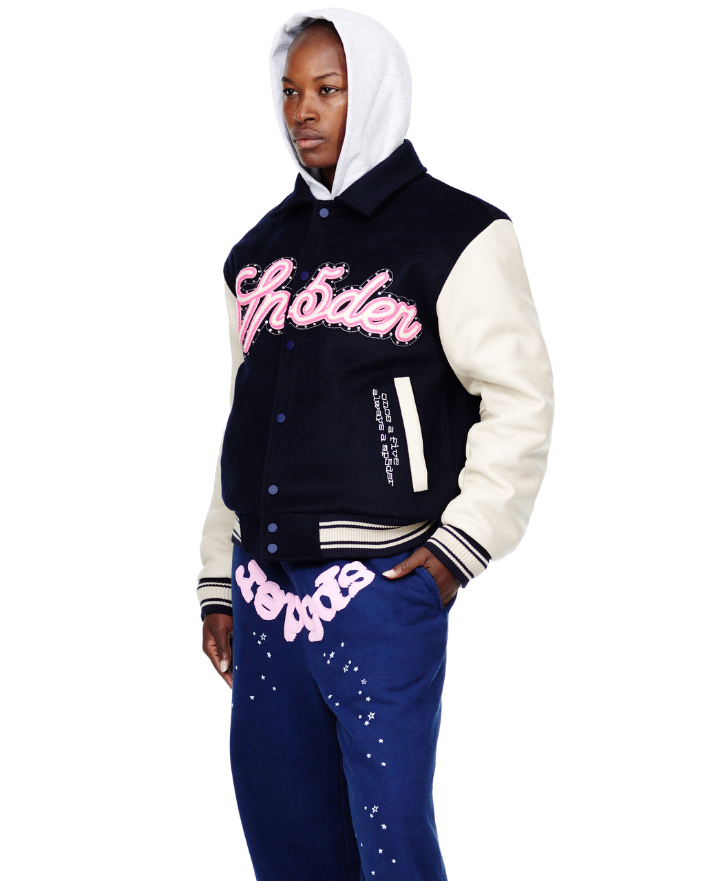 Man in a navy wool varsity jacket with cream cowhide sleeves, pink chenille patches, and a grey hoodie.