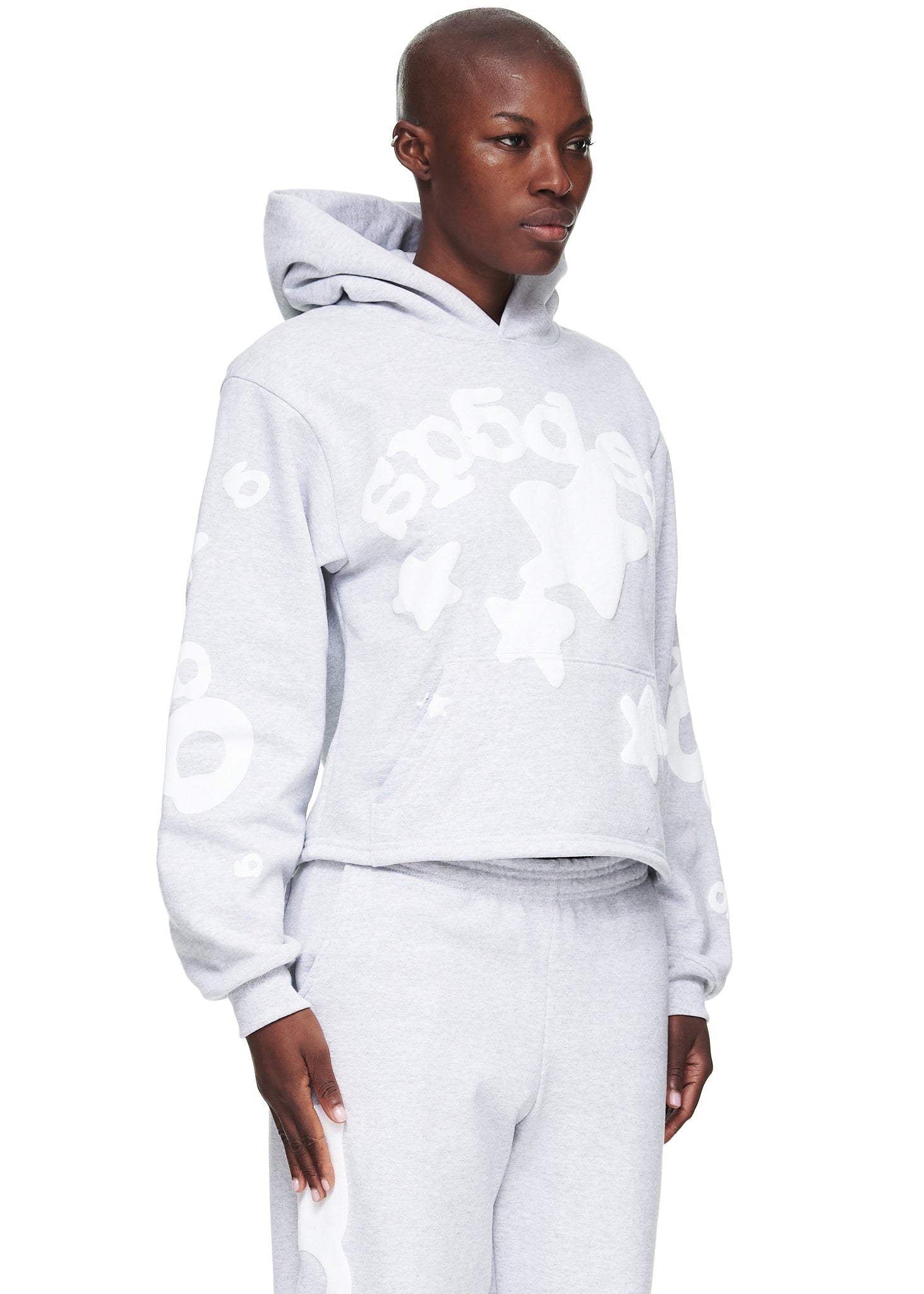 Woman in a light grey cropped fleece hoodie with white "SP5DER" and star puff print.