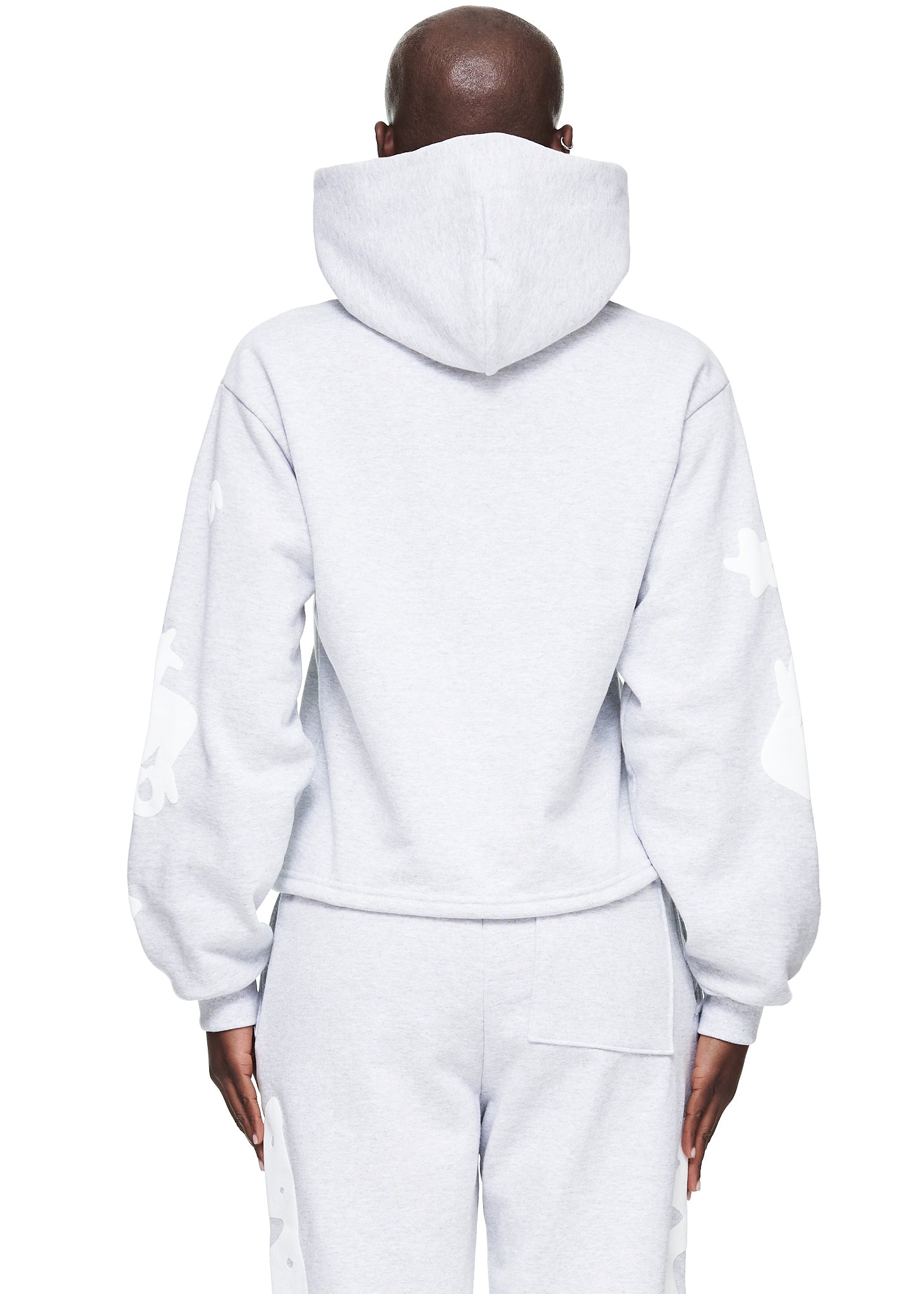 Back view of a model wearing a light gray cropped fleece hoodie with white puff print designs on the sleeves.