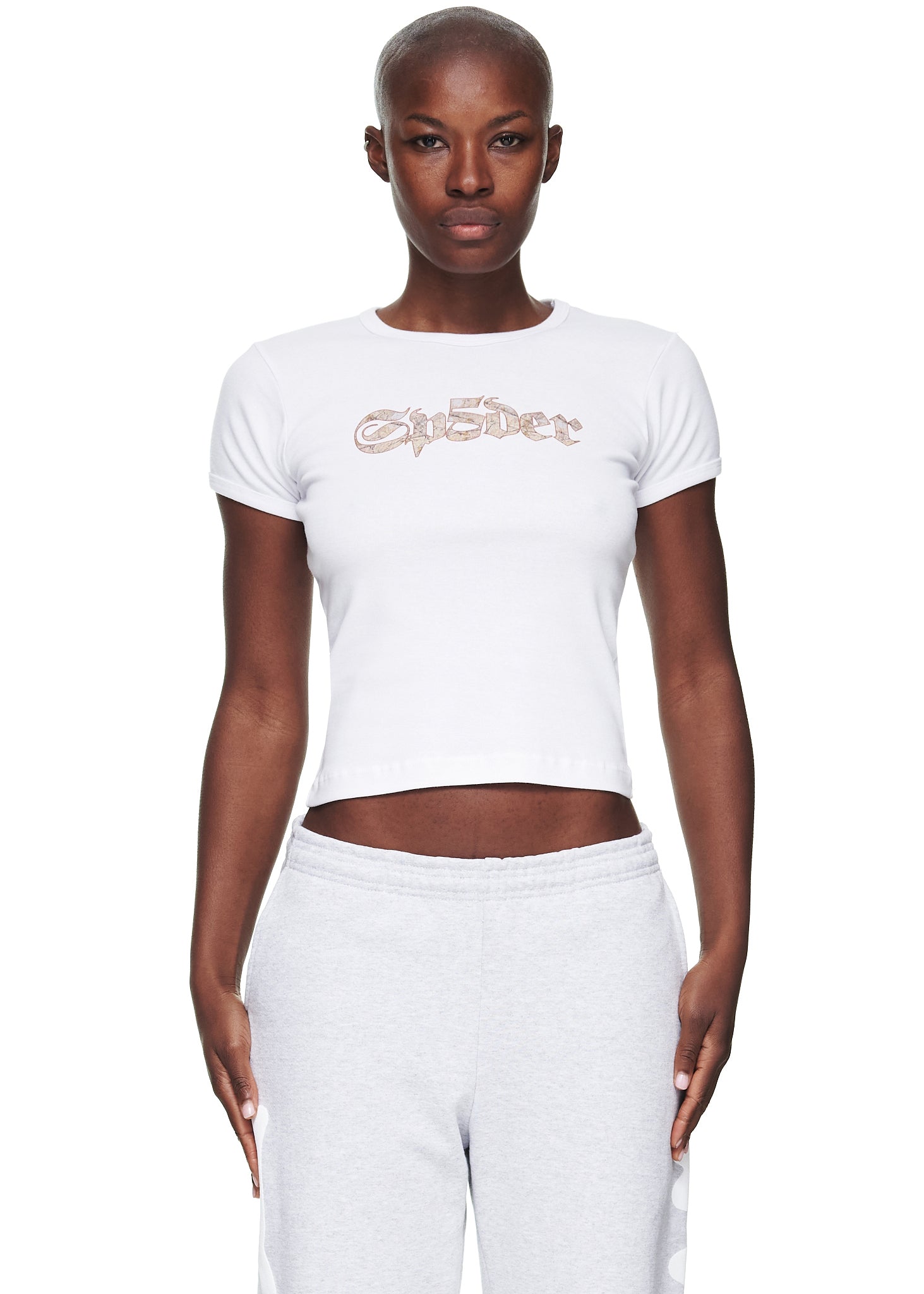 Female model in a white cropped fitted cotton baby tee with a graphic print, paired with light grey sweatpants.