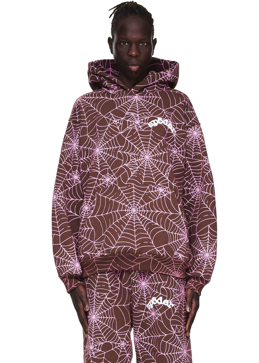 Male model in a brown AOP hoodie with pink cracked web print and "SP5DER" text.