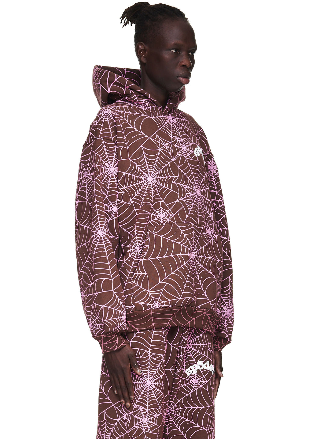 Male model in a brown AOP hoodie with pink cracked web print and 'SP5DER' text.