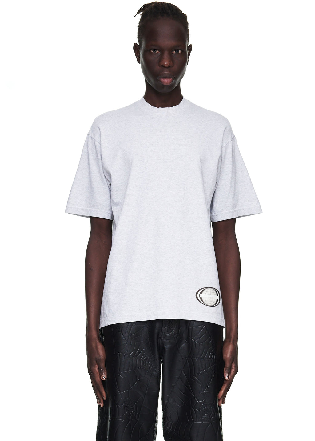 Male model wearing a heather grey 100% cotton standard fit utility tee with a graphic print on the corner hem.