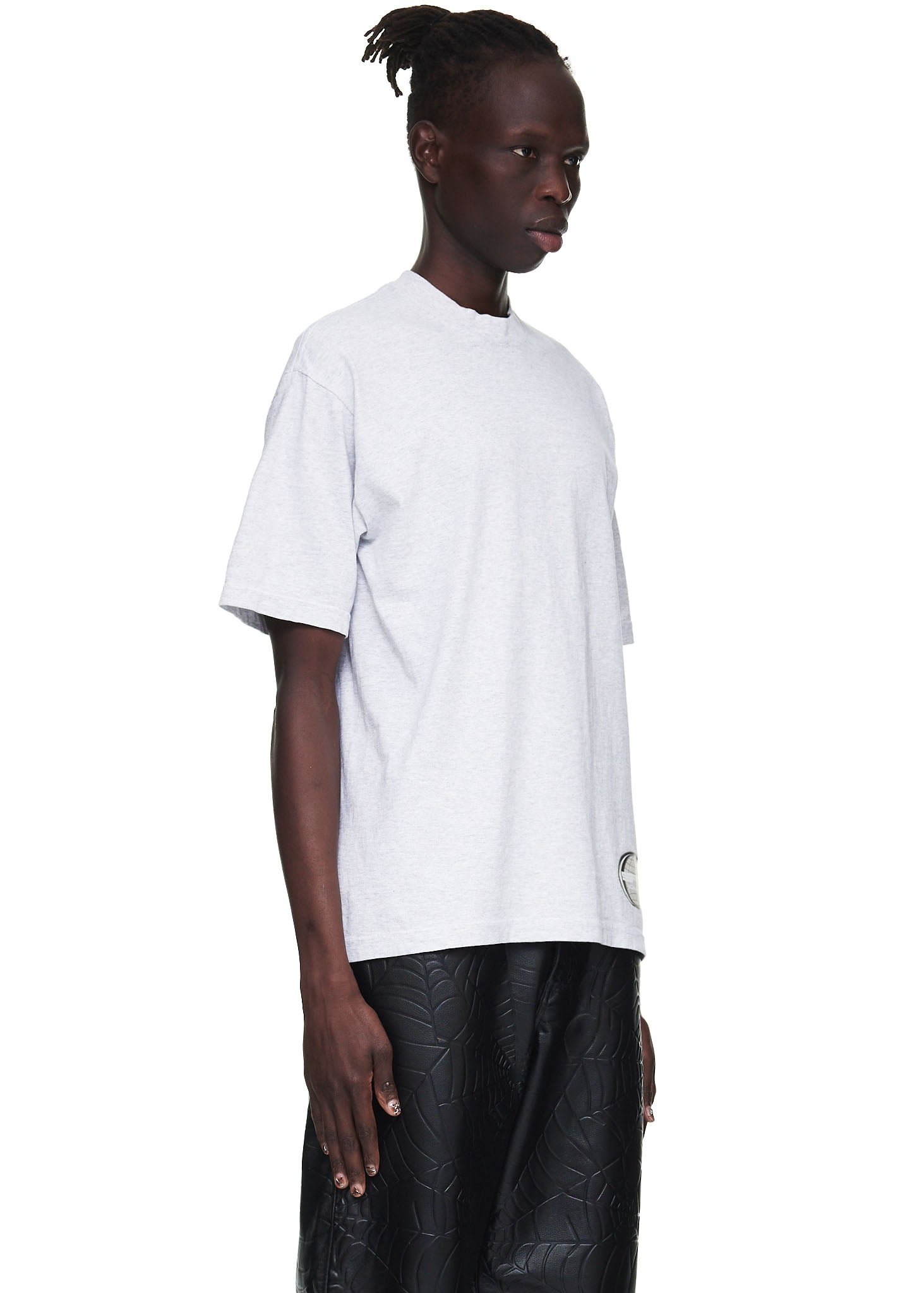 Male model in a heather grey 100% cotton utility tee with a graphic print on the corner hem.