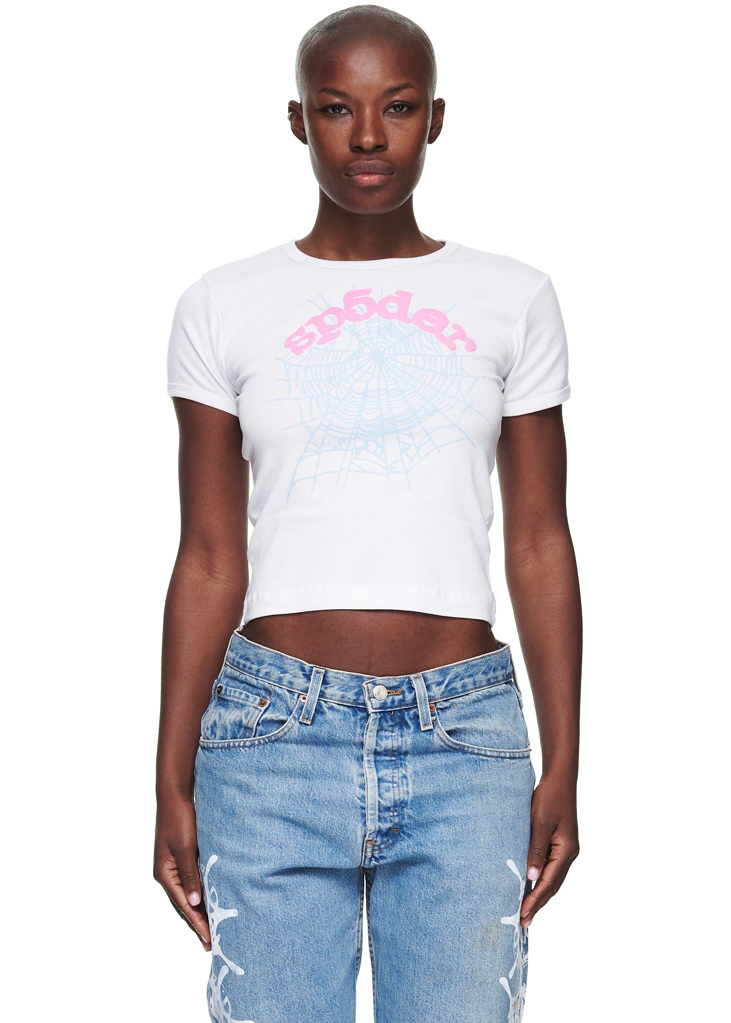Female model in white 100% cotton cropped baby tee with pink "sp5der" text and blue spider web graphic.