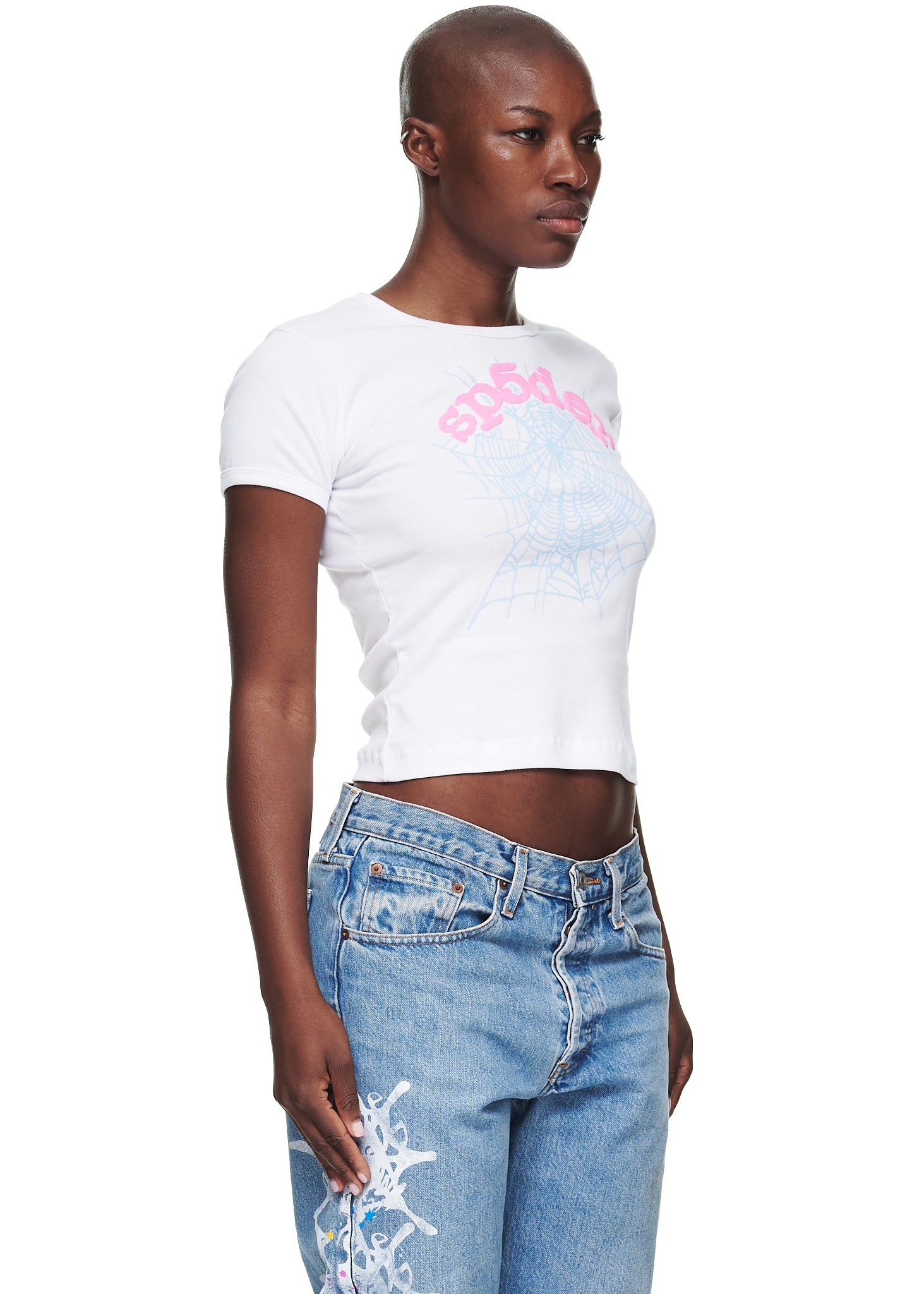 Female model in white cotton cropped tee with pink "sp5der" text and blue spiderweb graphic.