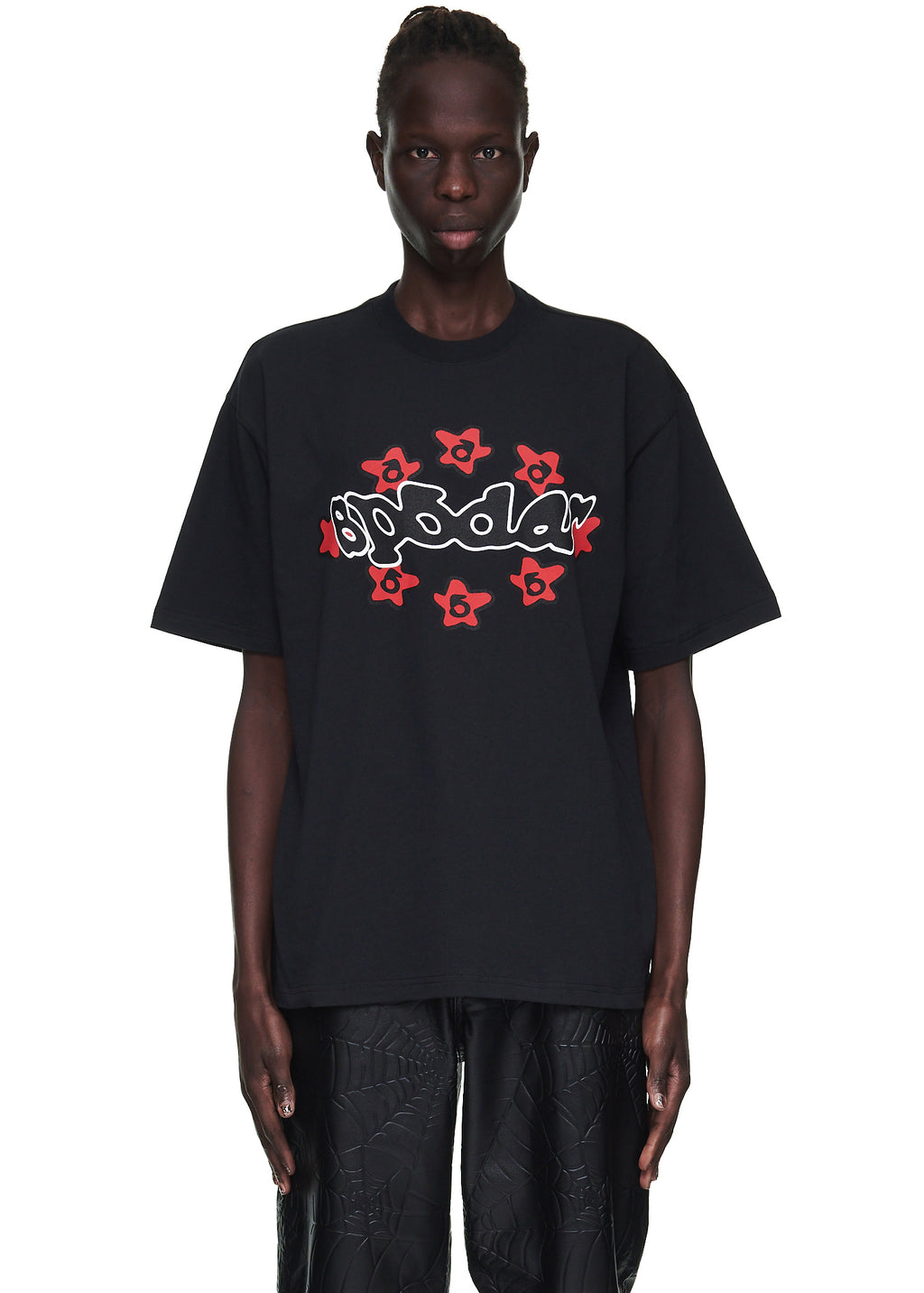 Male model in black cotton SP5DER tee with warped graphic print and red stars.