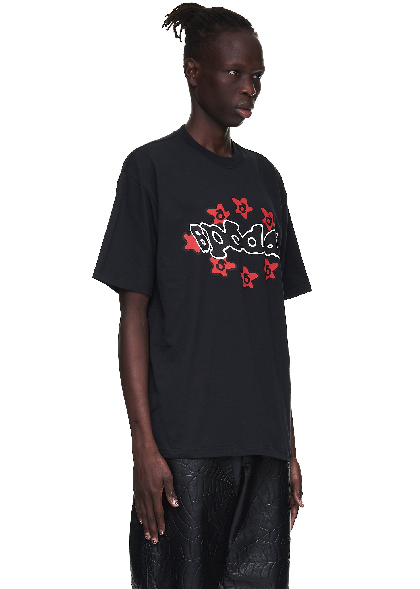 Male model in a black 100% cotton SP5DER tee with a red and white graphic print.