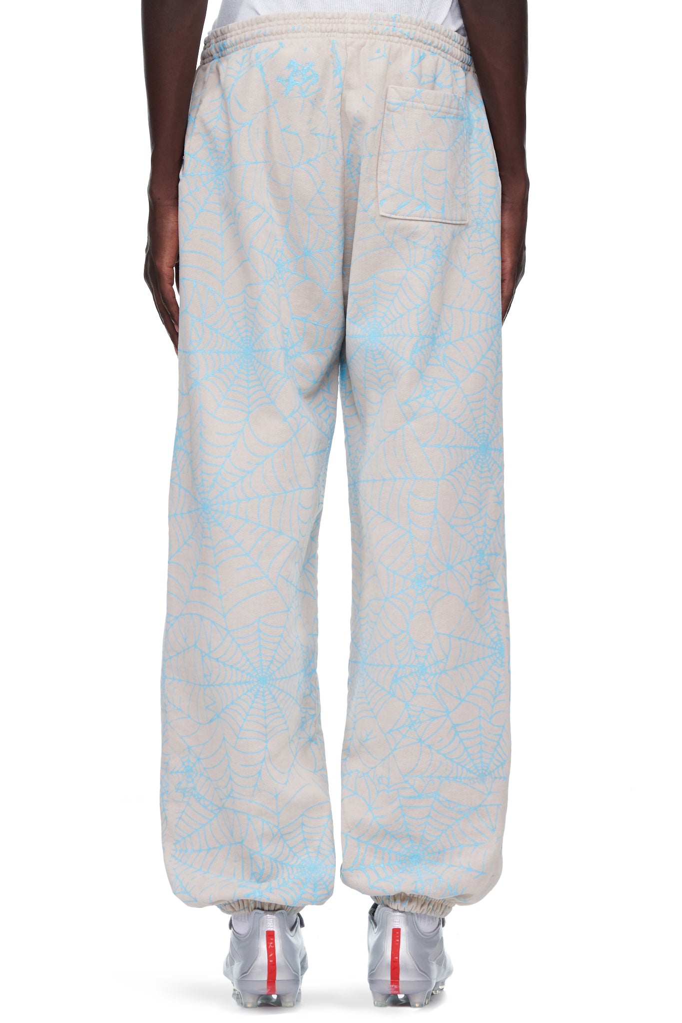 Beige 23oz fleece sweatpants with all-over cracked blue web print and "SP5DER" text.