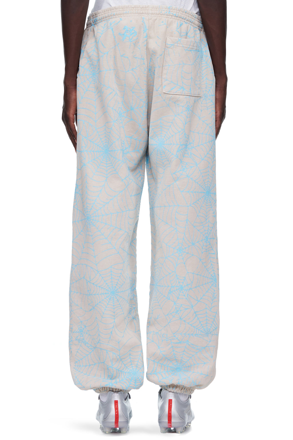 Beige 23oz fleece sweatpants with all-over cracked blue web print and "SP5DER" text.