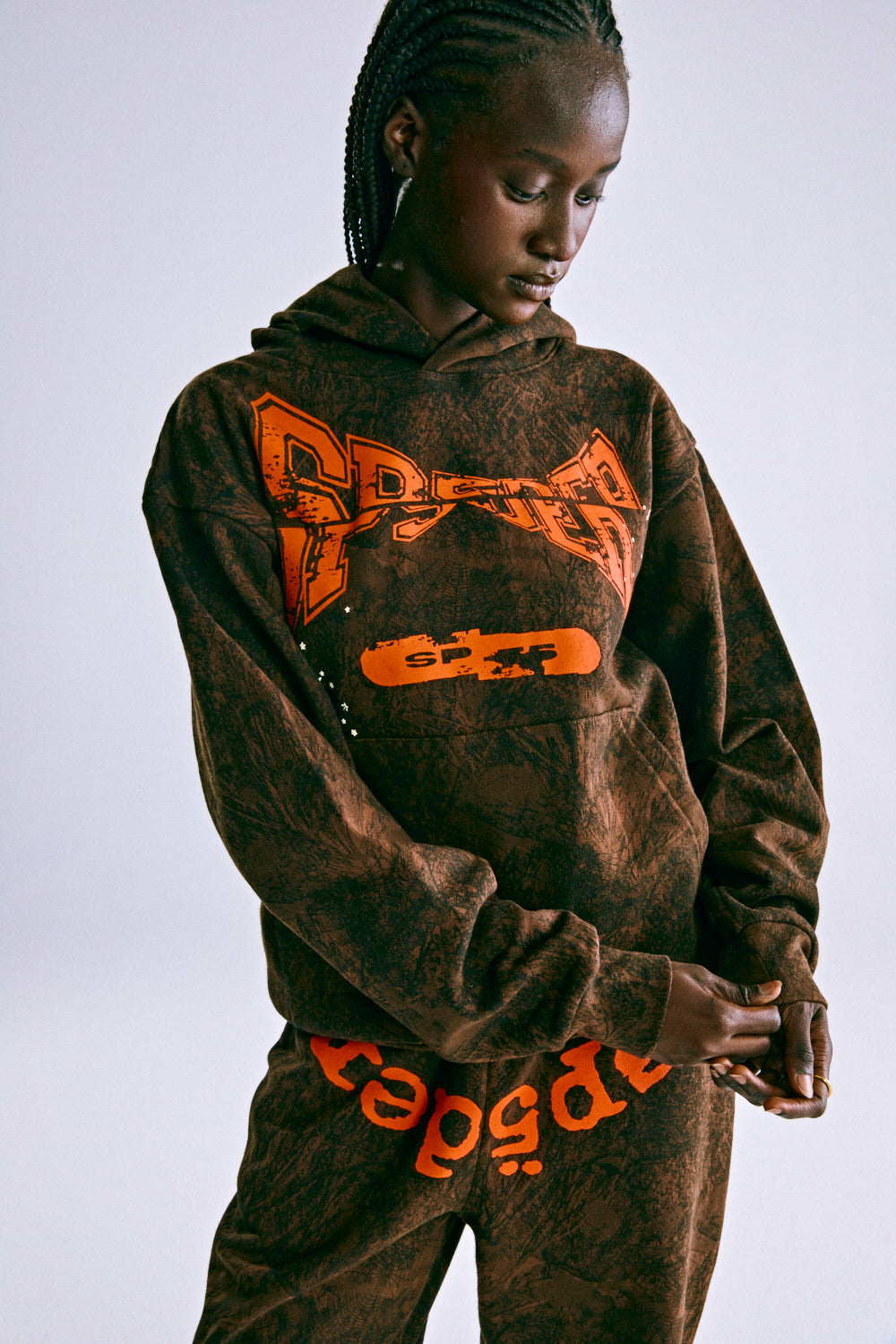 Brown tree camo hoodie with orange "SP5DER" chest print and matching sweatpants.