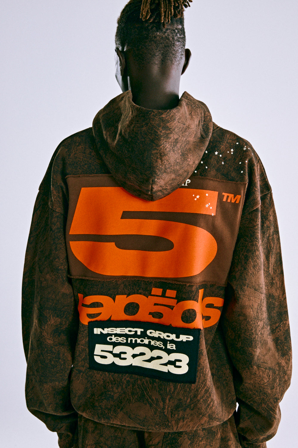 Brown tree camo hoodie with large orange '5' and 'SP5DER' text, custom racing patch on back.