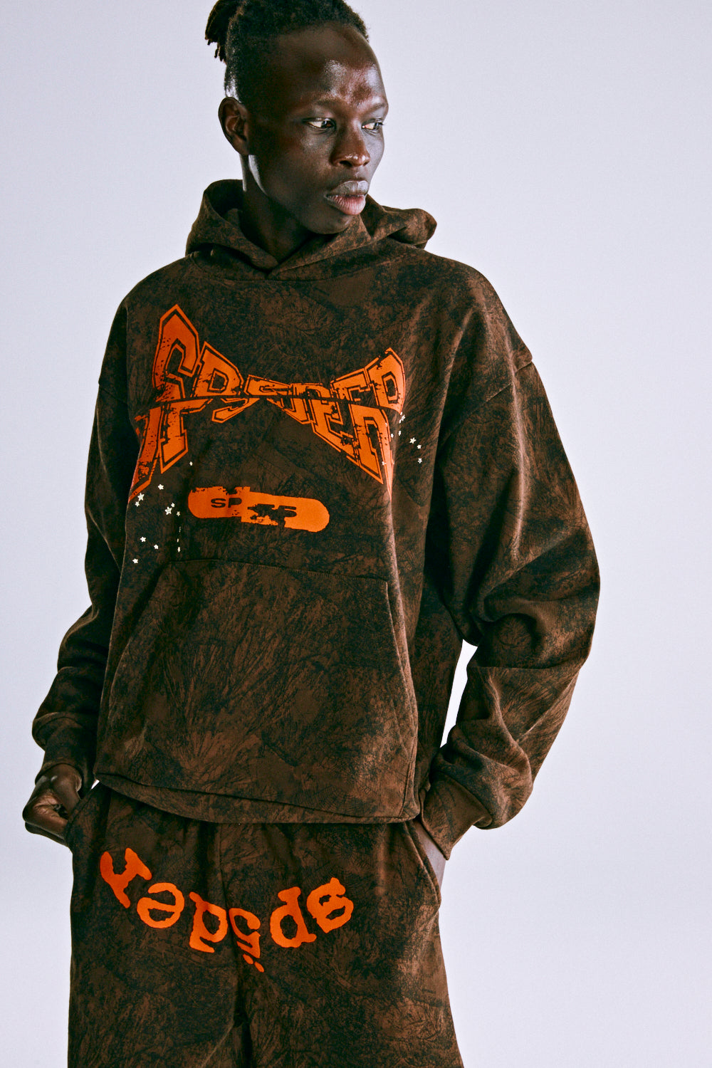 Brown tree camo hoodie with orange "SP5DER" text, matching sweatpants.