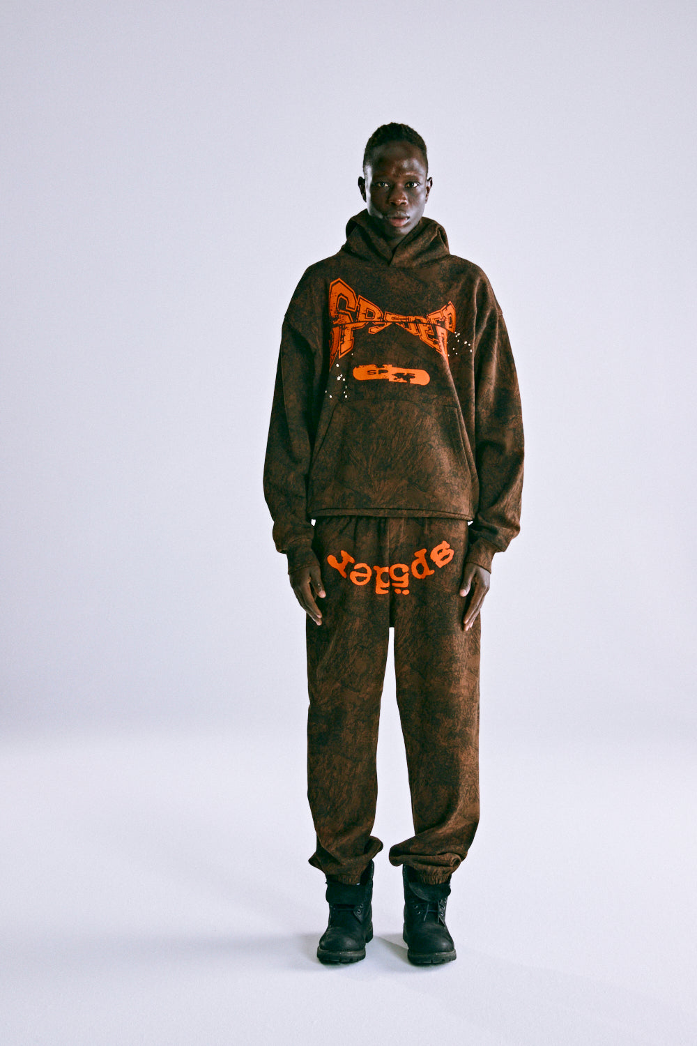 Man in T&F TREE CAMO HOODIE and sweatpants, featuring orange puff print 'SP5DER' text and custom racing patch.