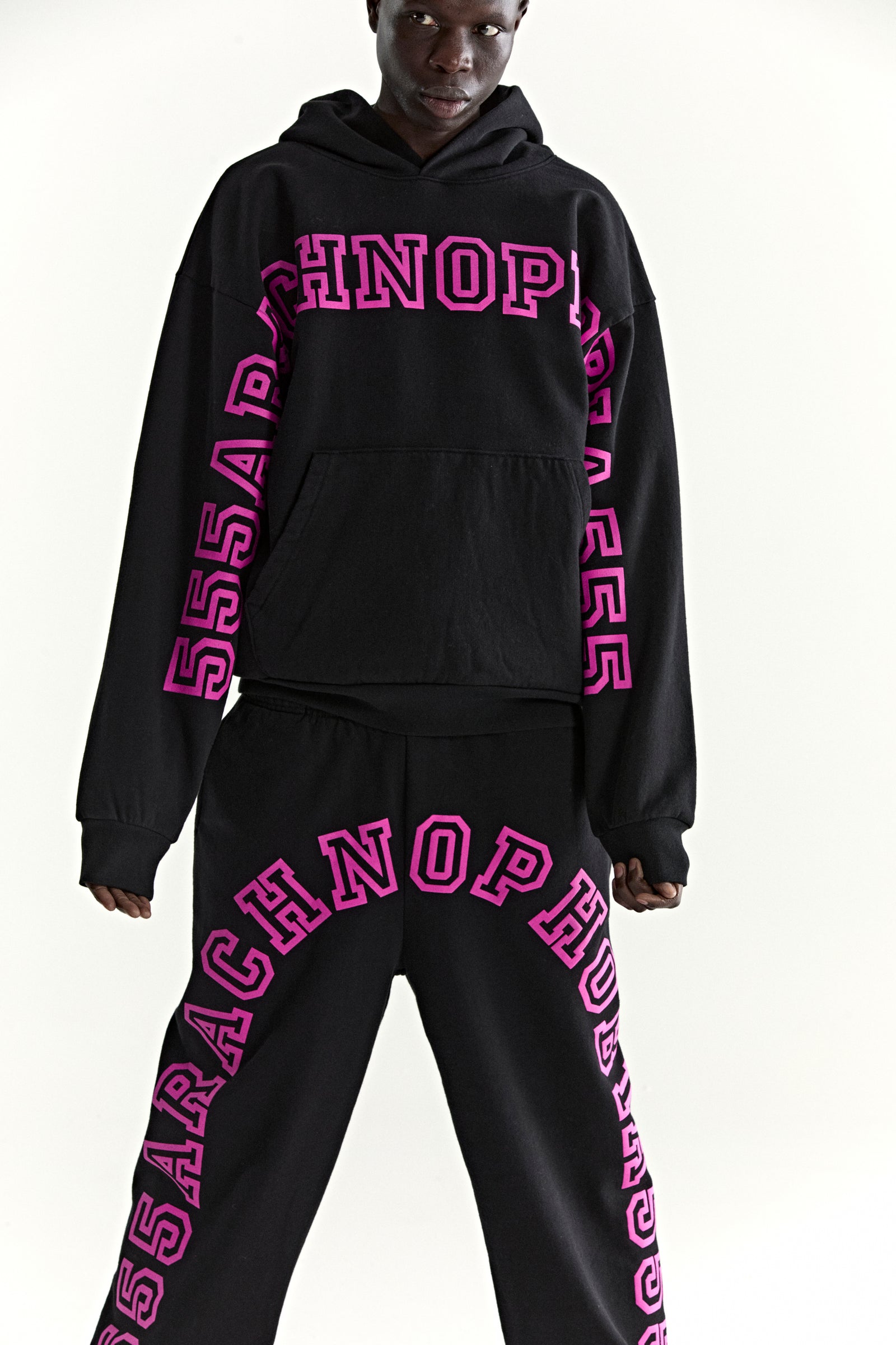 Black ARACH HOODIE and sweatpants set with bold pink puff print text on chest, arms, and legs.
