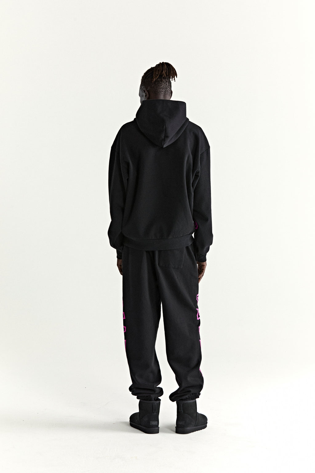 Black 13oz cotton fleece ARACH hoodie and sweatpants with pink text print, worn from behind.