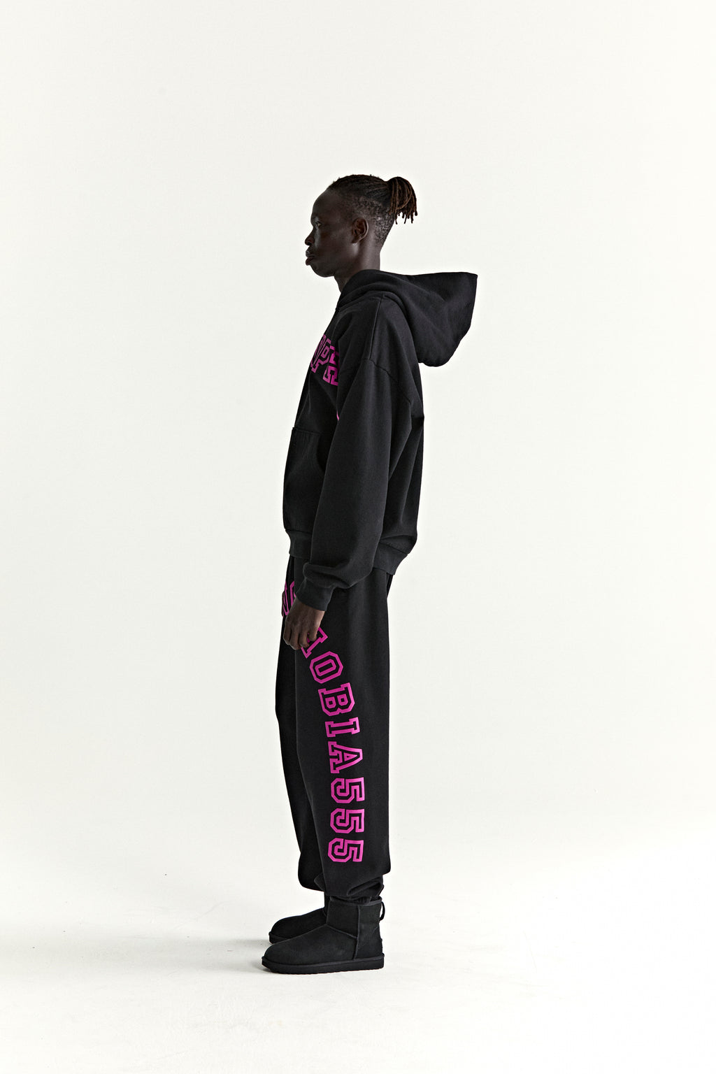 Black cotton fleece ARACH hoodie and sweatpants with pink text print, worn by a model in profile.