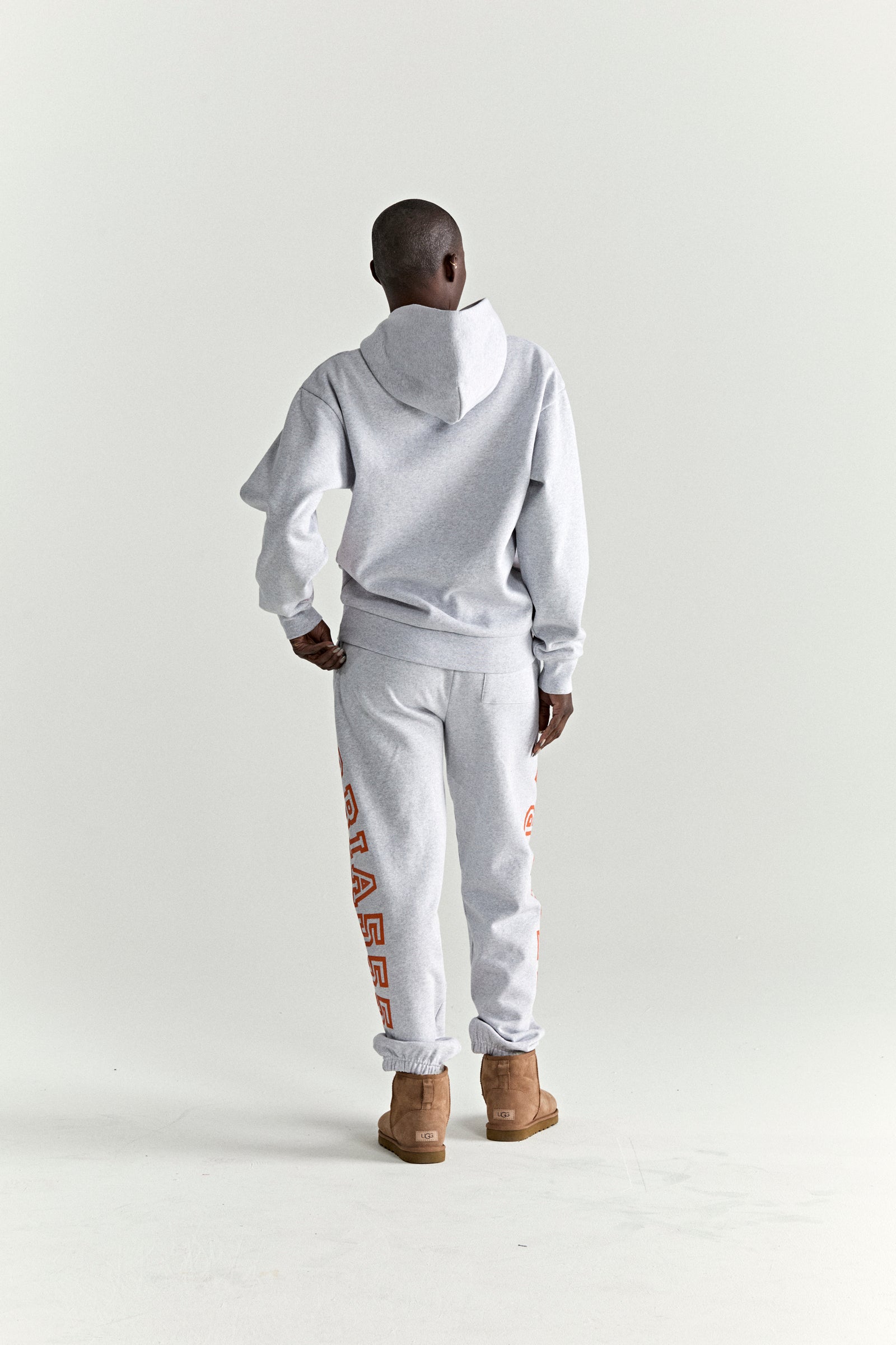 Gray ARACH hoodie and sweatpants set with orange text print, worn by a person from behind.