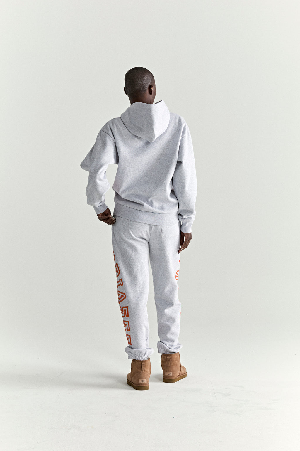 Gray ARACH hoodie and sweatpants set with orange text print, worn by a person from behind.