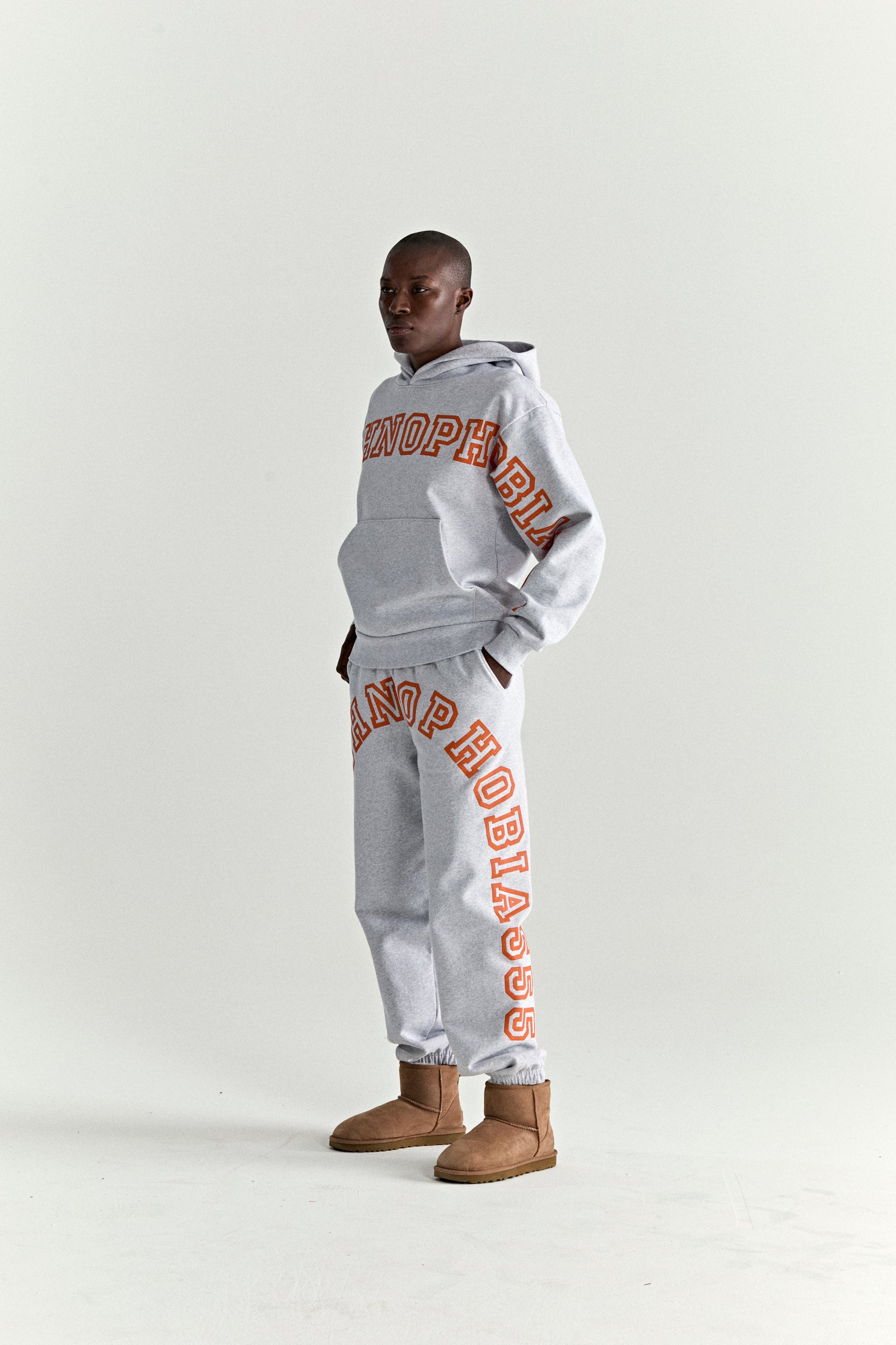 Gray 13oz cotton fleece ARACH HOODIE and sweatpants with orange puff print text, worn by a model.